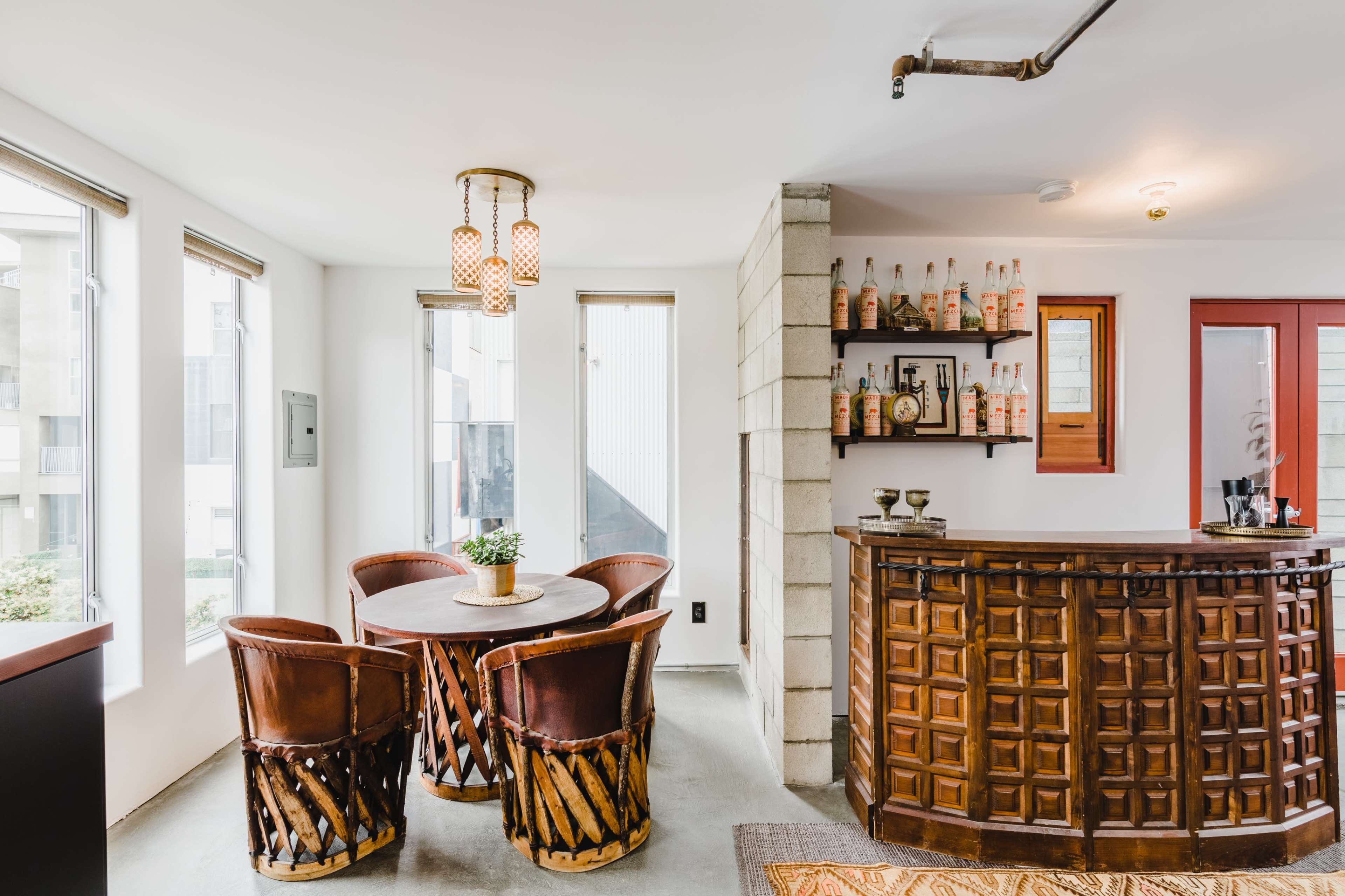 A modern interior with a wooden reception desk, a small round dining table surrounded by four leather chairs, and shelves displaying bottles and decorative items.