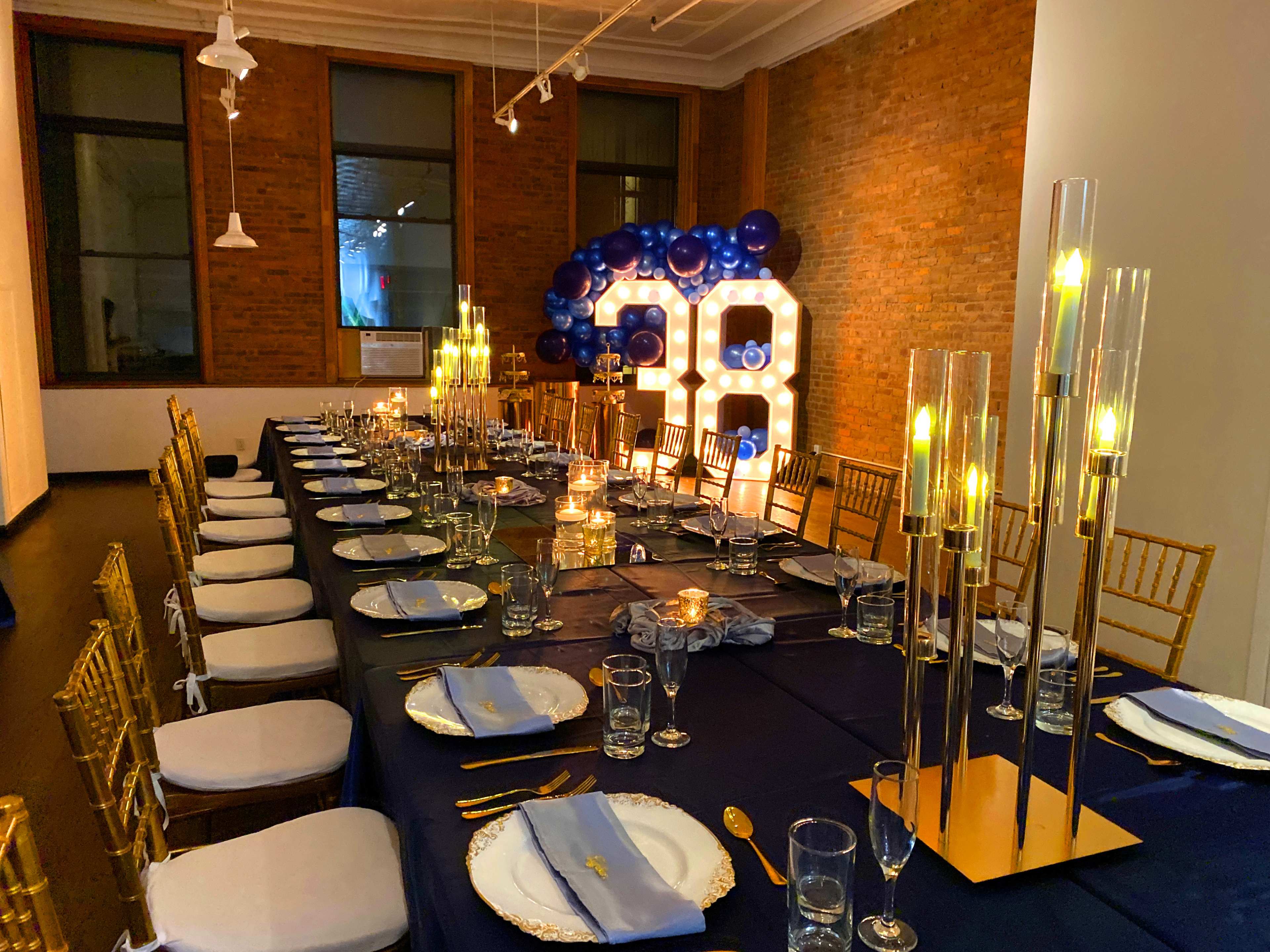 A long dining table is elegantly set for a celebration, complete with candles, glassware, and gold-accented décor, with a large illuminated "30" display in the background.