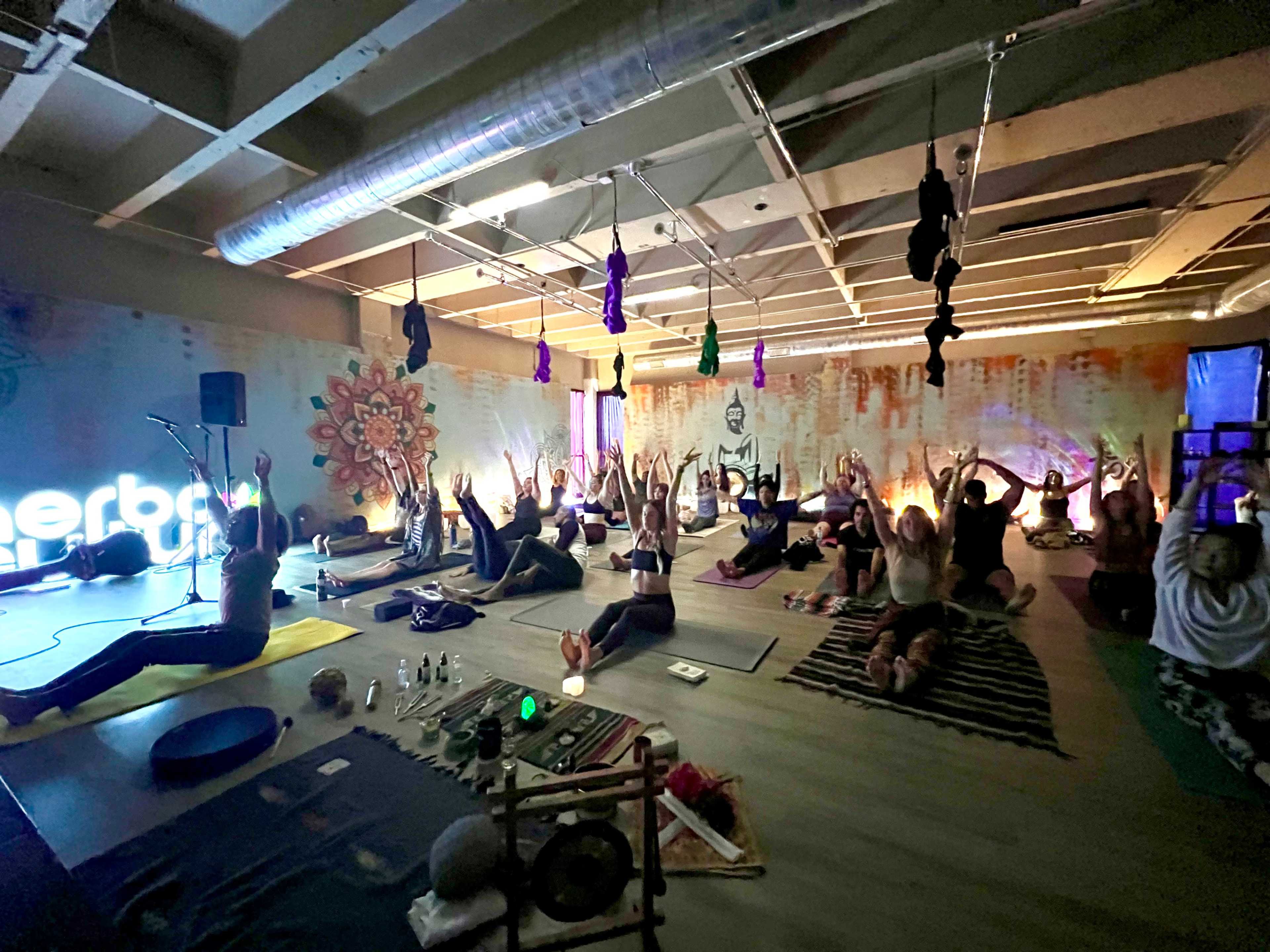 A group of people is practicing yoga in a dimly lit studio with various props and colorful decorations on the walls.