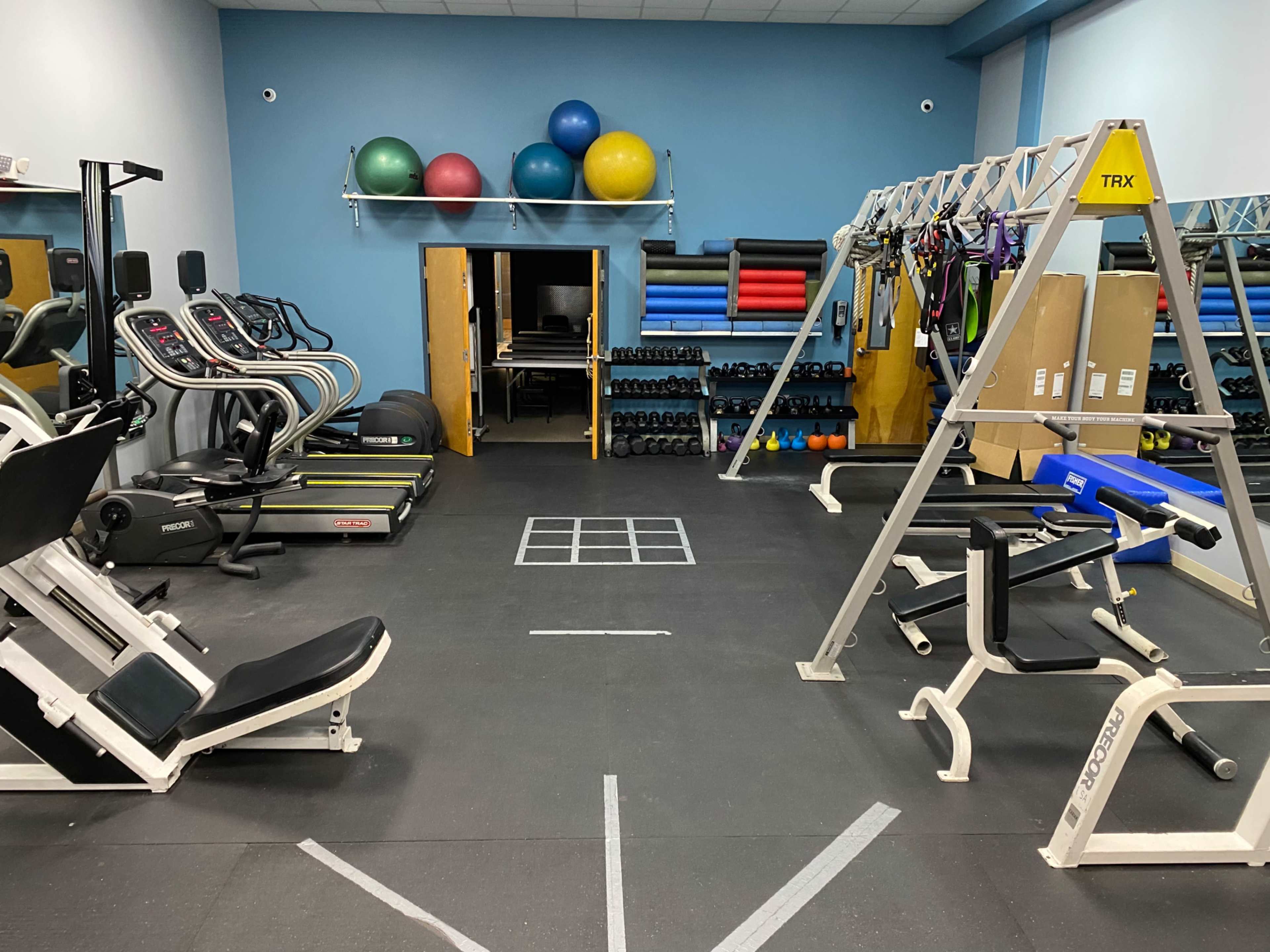 A fitness gym with various exercise equipment, including cardio machines, weights, and a TRX suspension training setup.