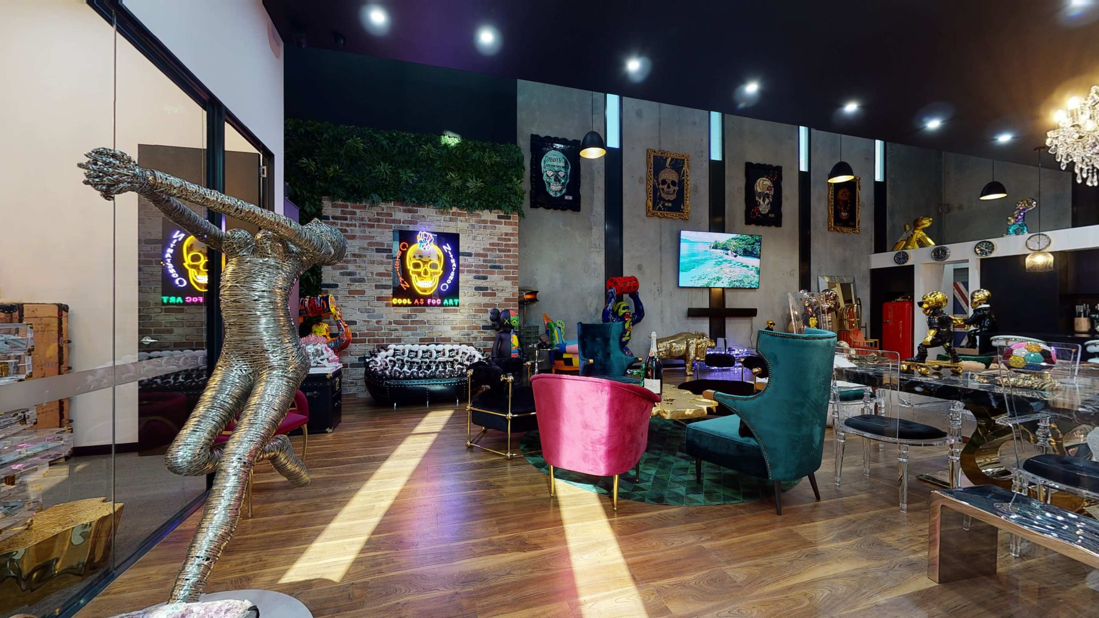 The image shows a modern interior space with colorful furniture, a metallic sculpture, and wall art, featuring a mix of seating areas and decorative elements.