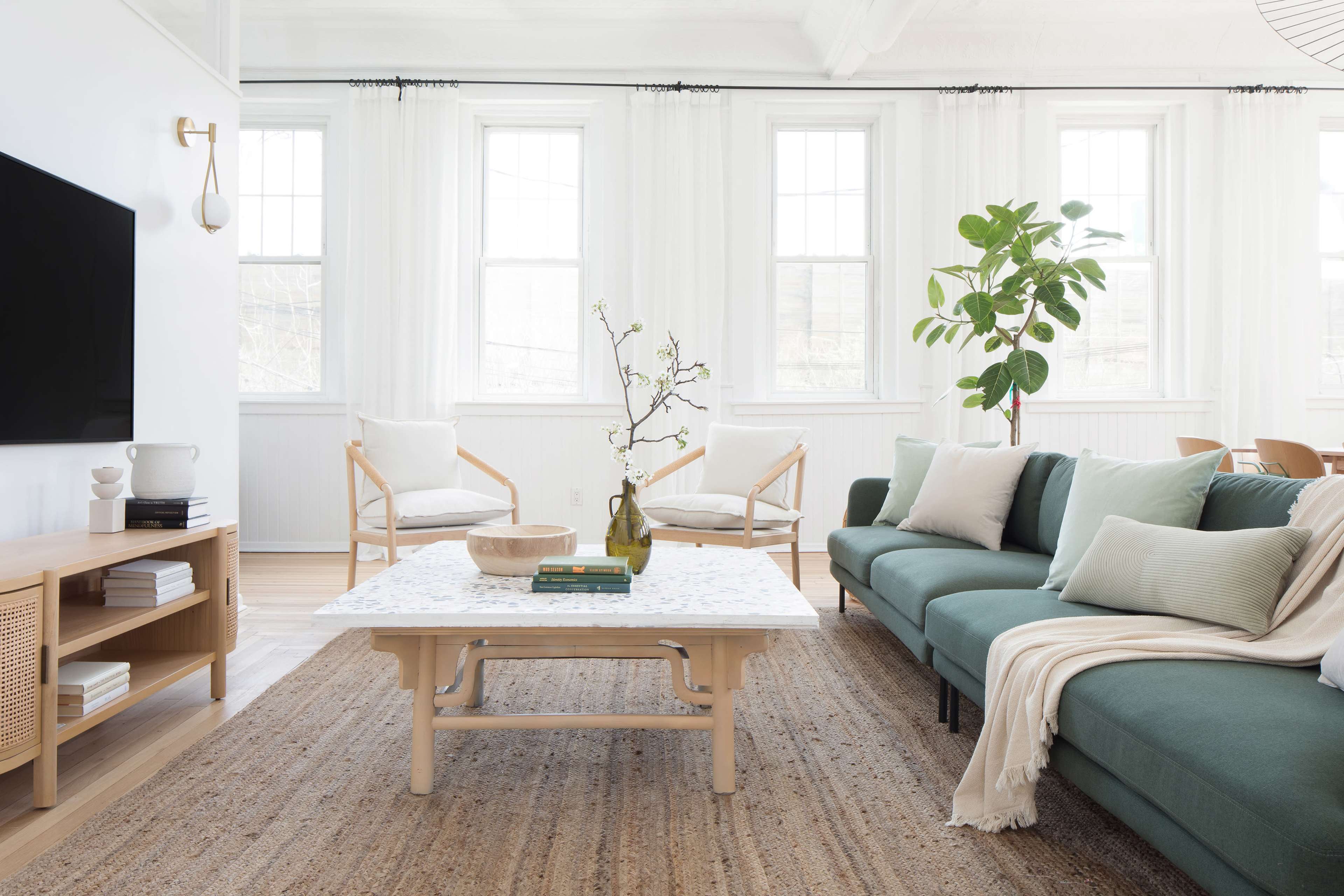 The living room features a green sofa, a wooden coffee table with a plant centerpiece, two armchairs, and large windows allowing natural light to enter.