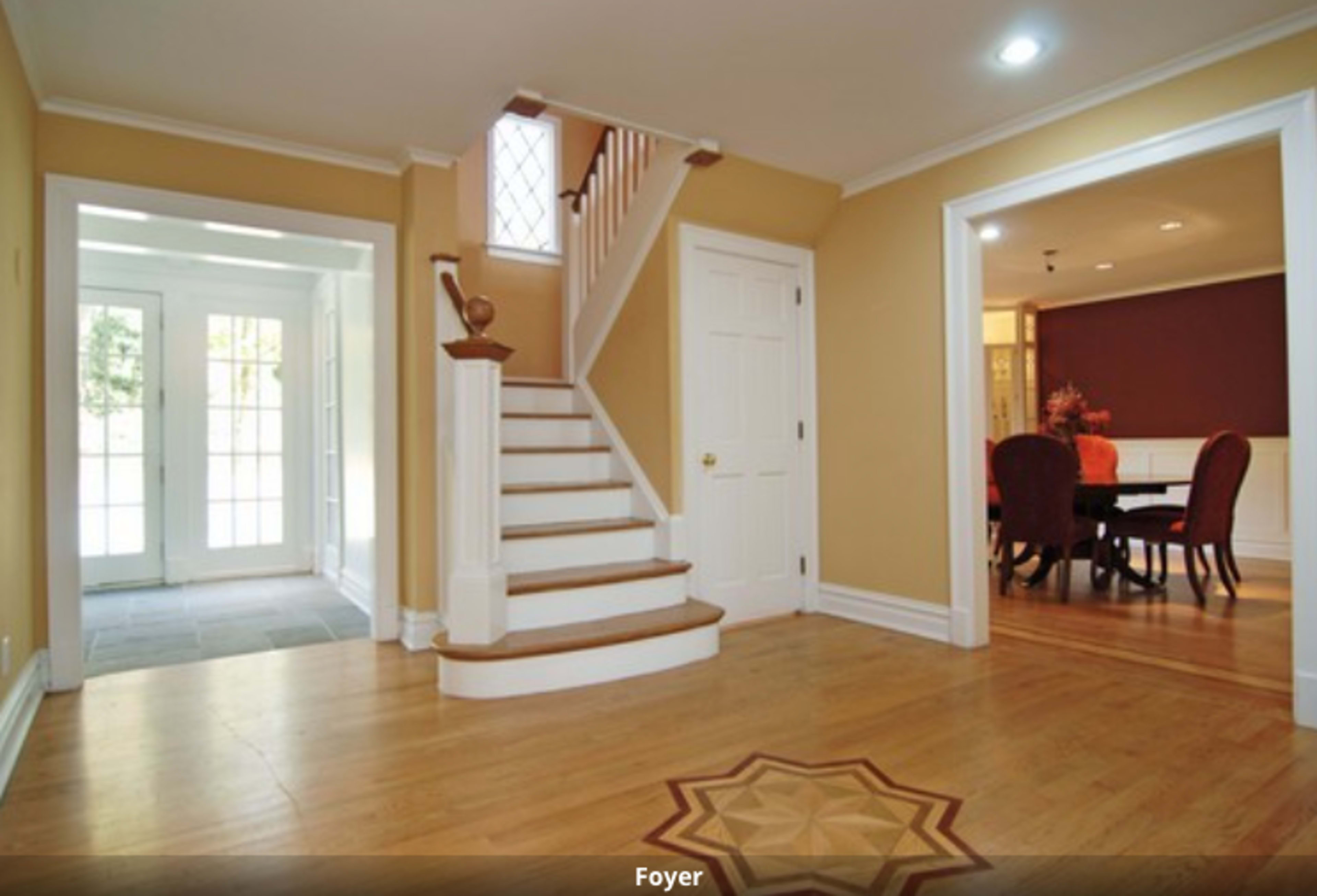A foyer with a staircase leading to the upper level and a view of a dining area through an open doorway.