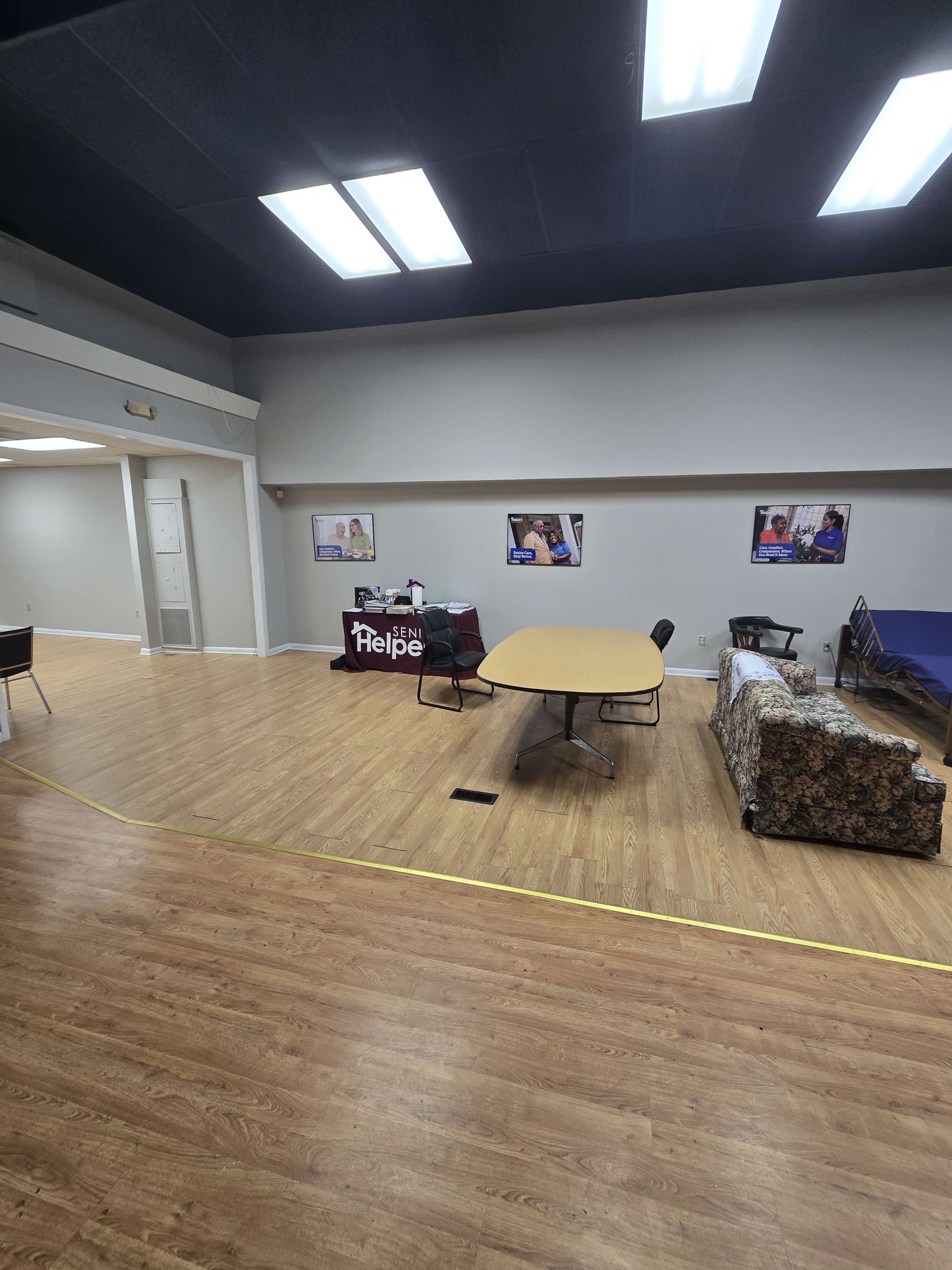 The image shows a spacious room with a large round table, a couch, and a display table labeled "Help," surrounded by light-colored walls and wooden flooring.