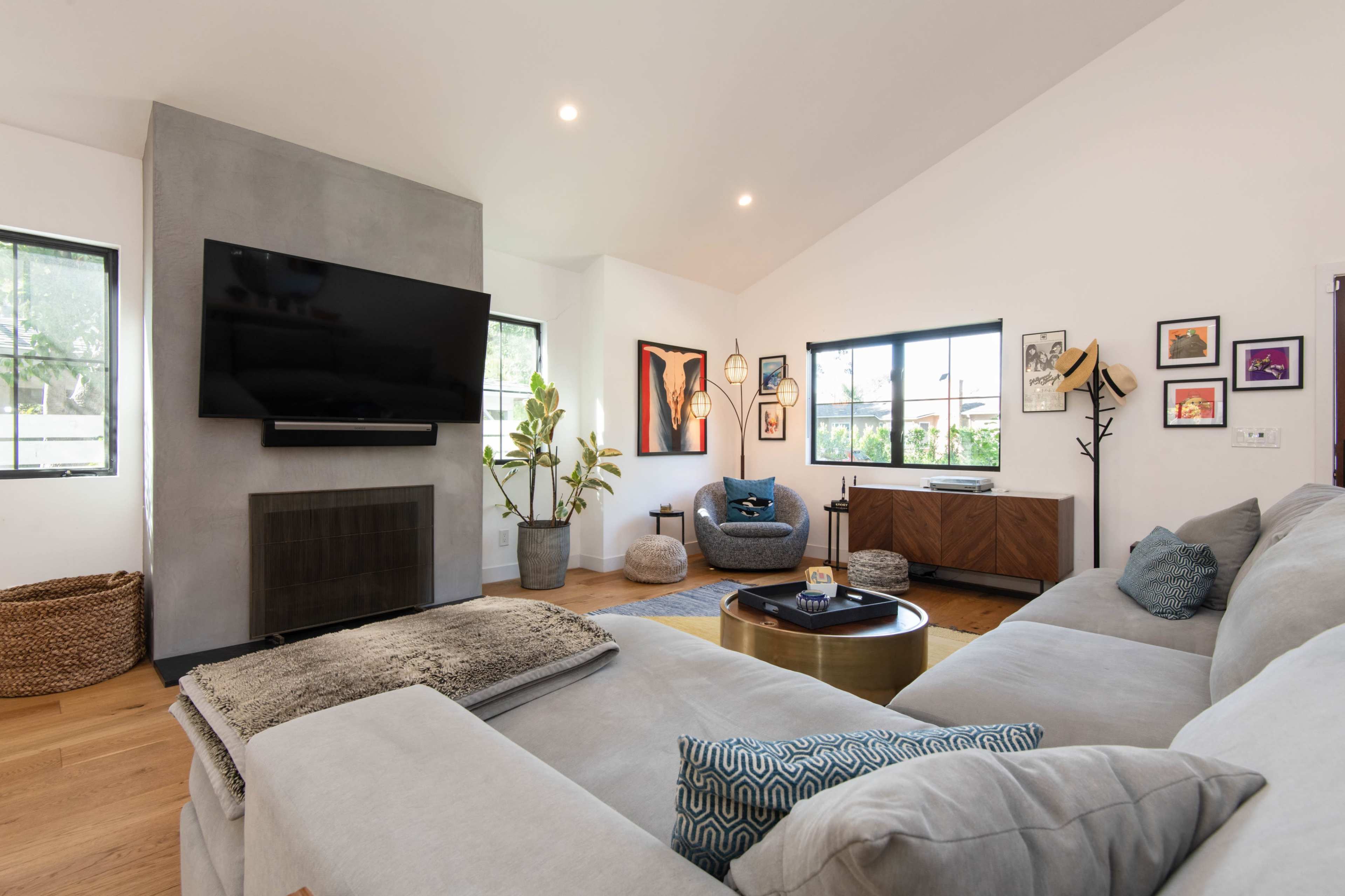 A modern living room with a sectional sofa, a mounted television, and a coffee table surrounded by indoor plants and decorative artwork on the walls.