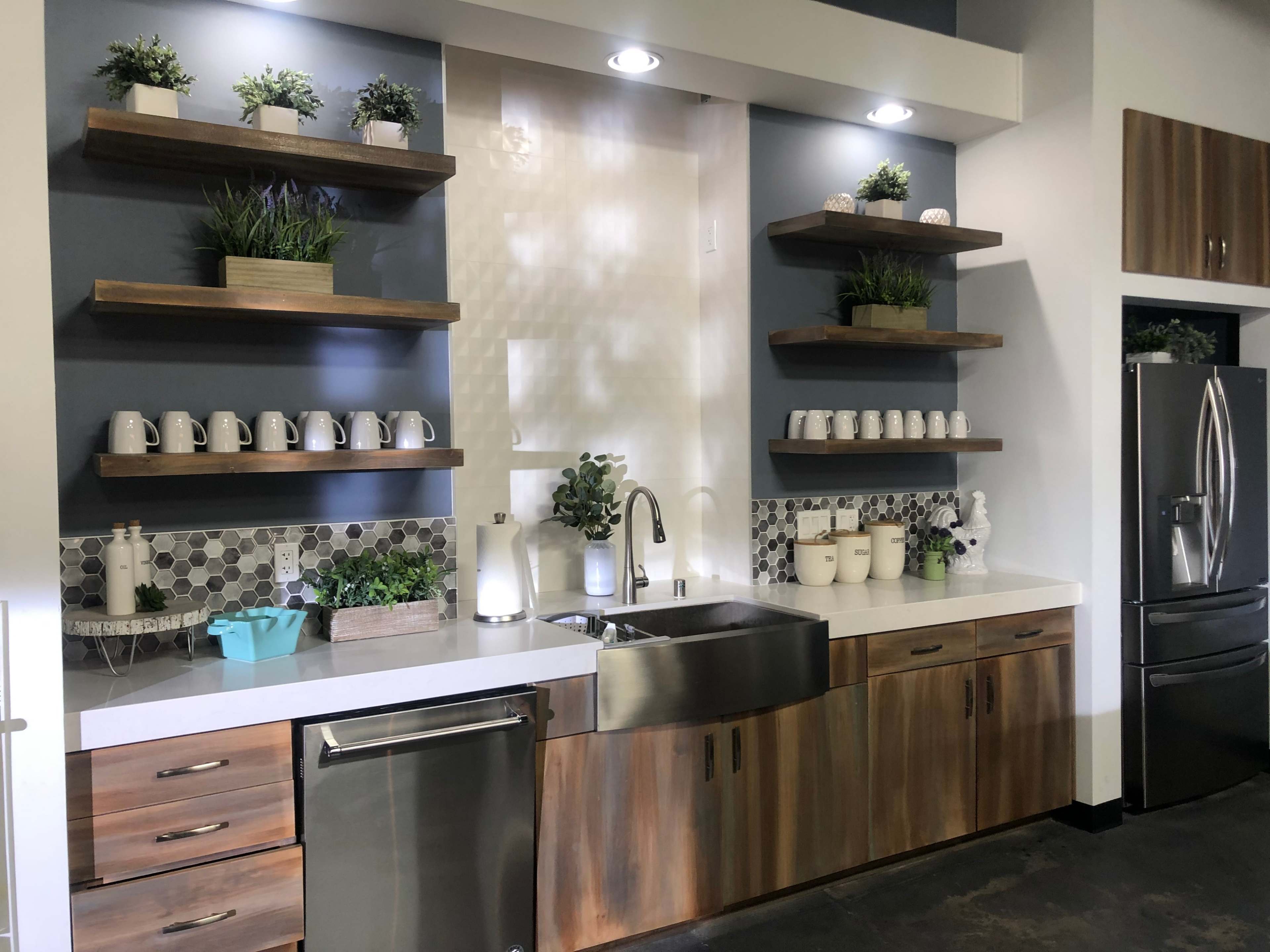 A modern kitchen featuring a stainless steel sink, wooden cabinetry, and open shelving adorned with potted plants and white mugs.
