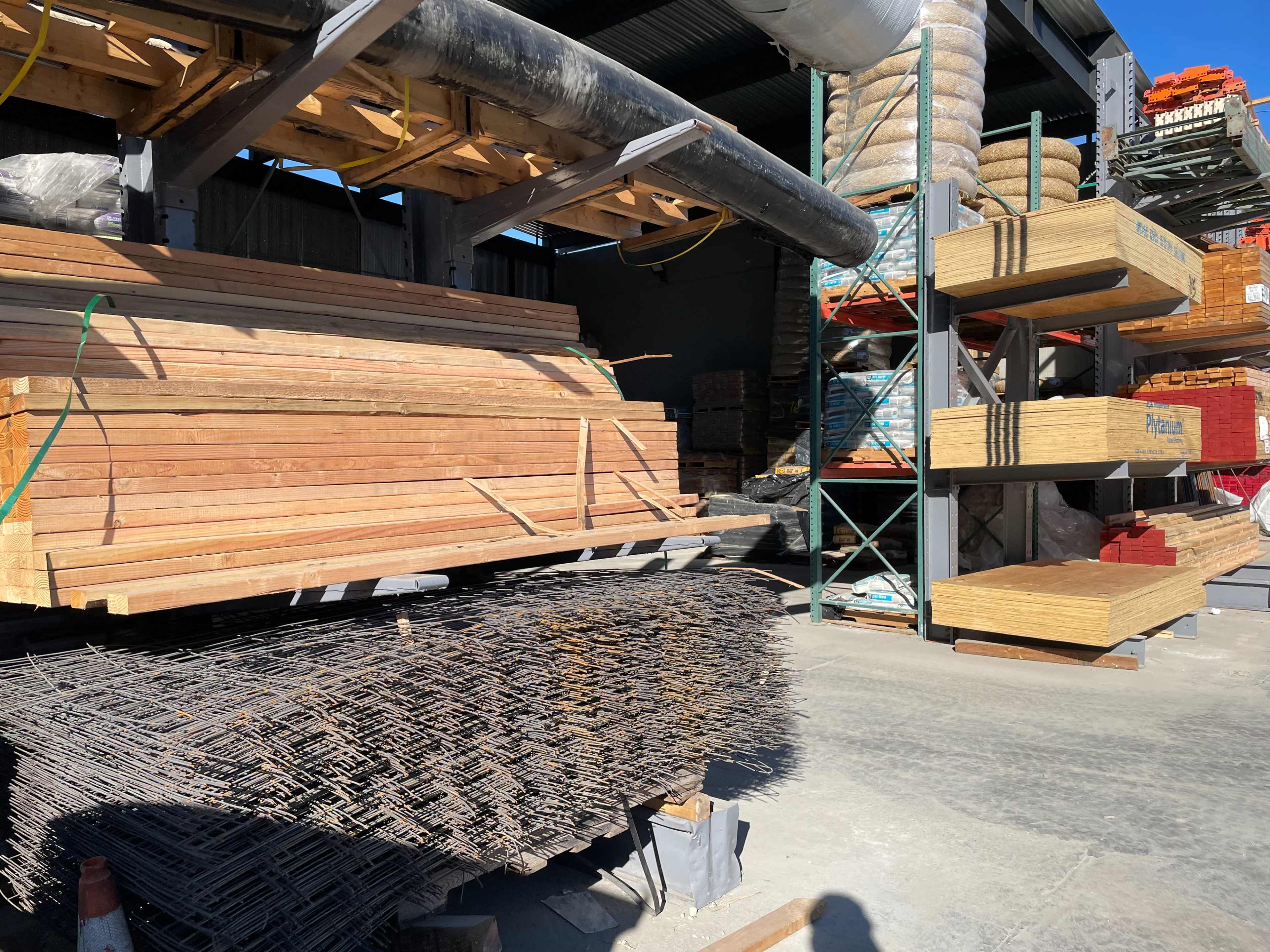 The image shows stacks of wooden planks and rebar stored in a construction supply yard.