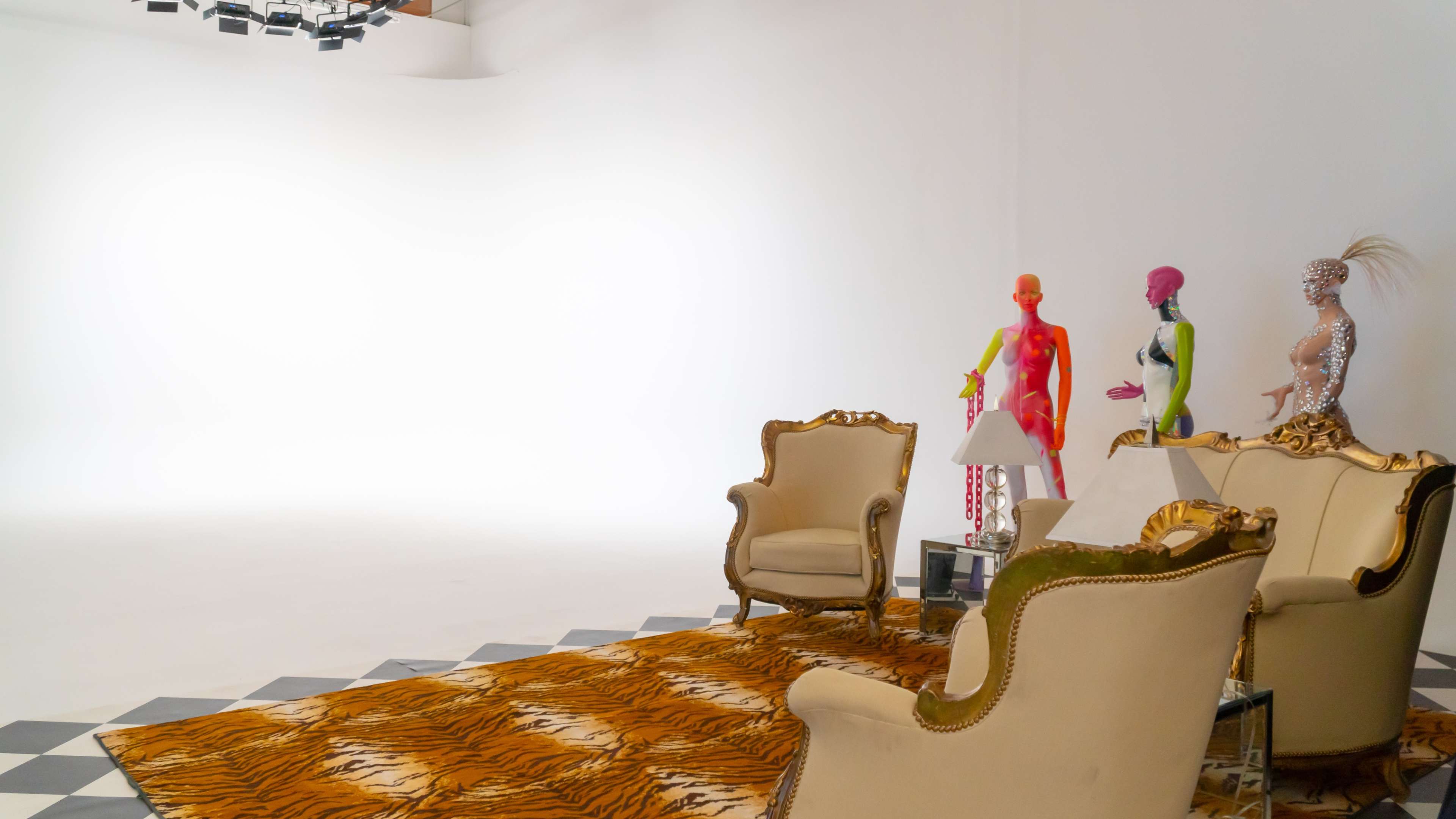 A spacious studio features ornate chairs on a patterned floor, with colorful mannequins positioned nearby against a white backdrop.