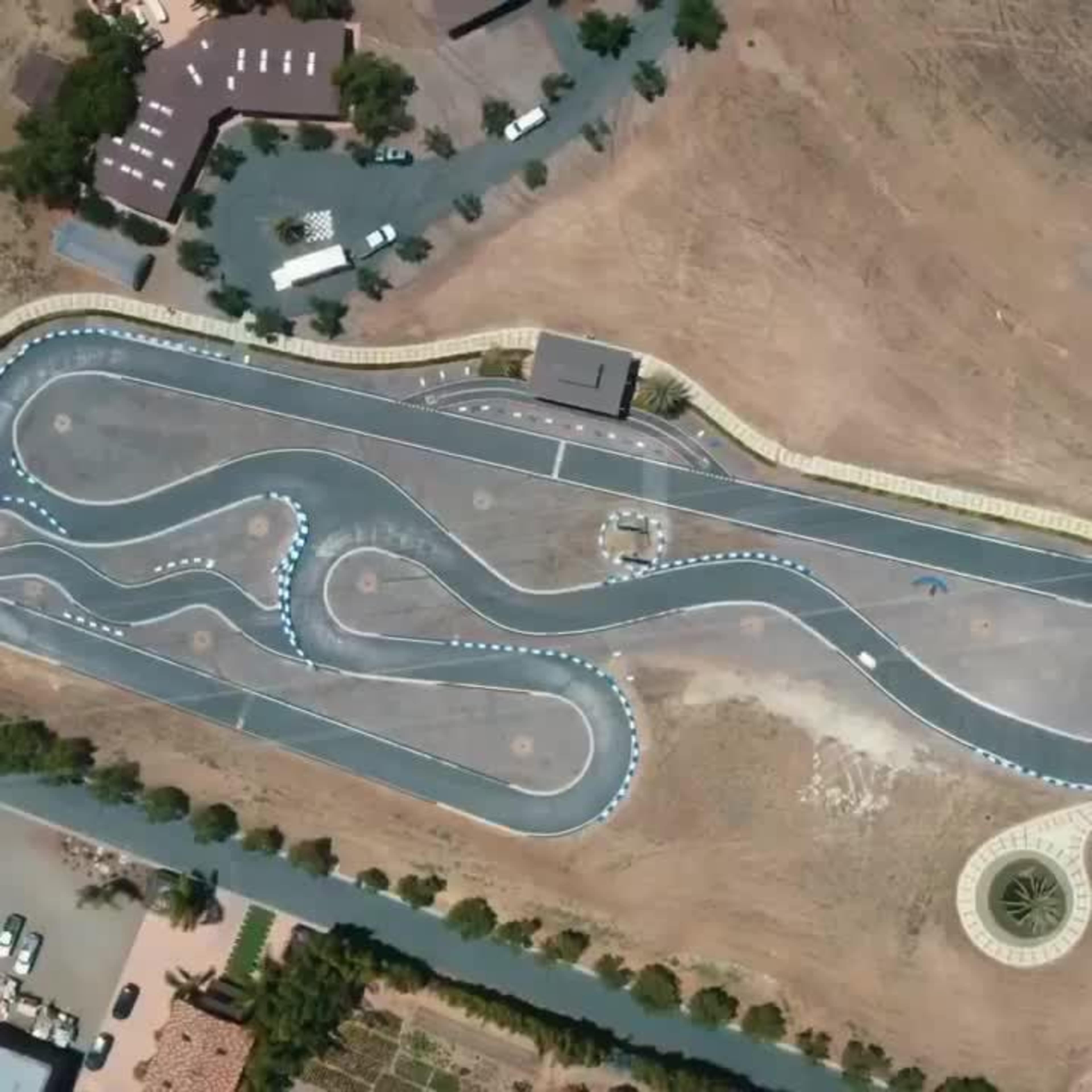 An aerial view of a winding go-kart track surrounded by sparse vegetation and a few structures.