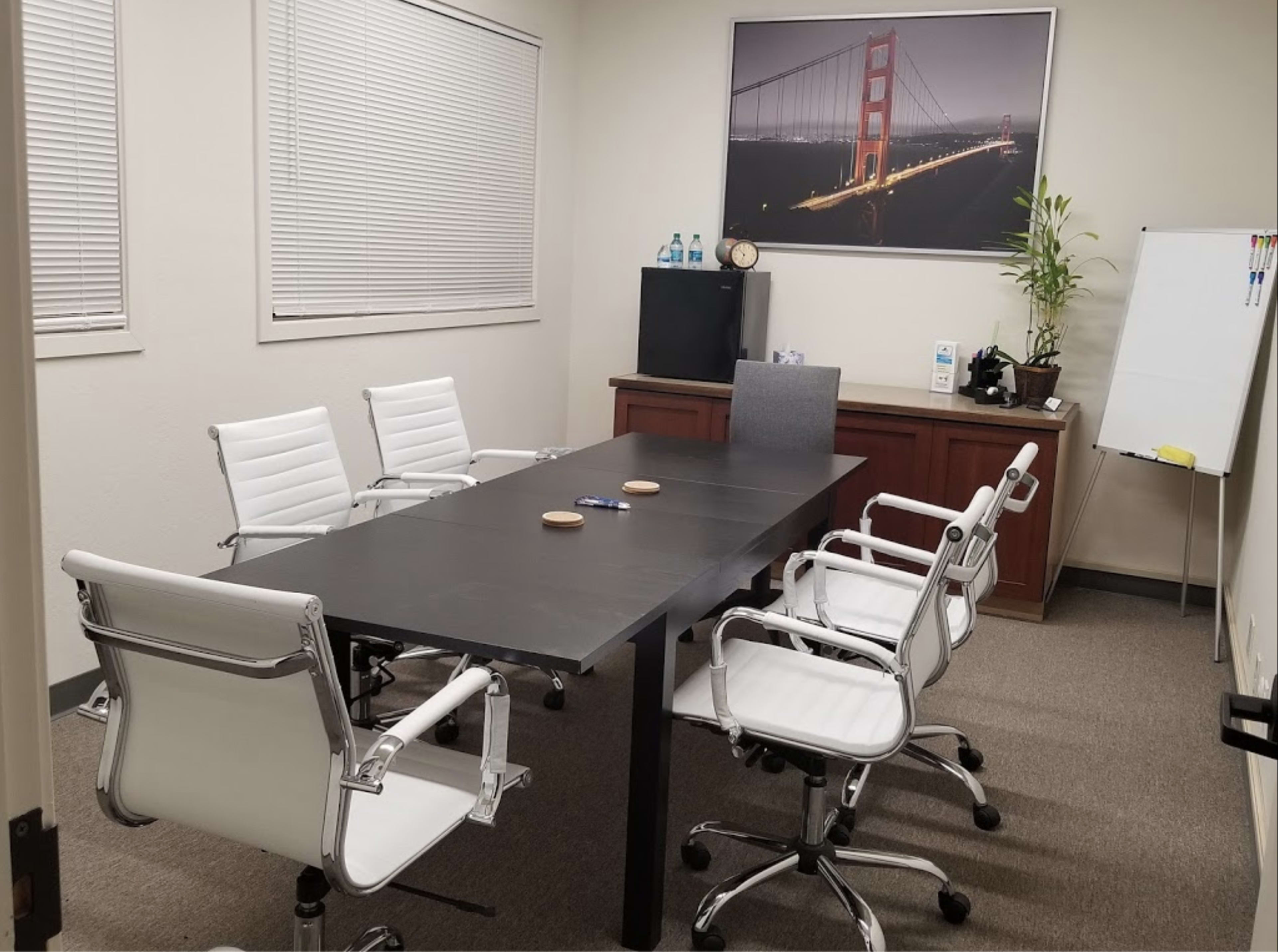 The image shows a conference room with a table surrounded by white chairs, a large photo of the Golden Gate Bridge on the wall, and a credenza in the corner.