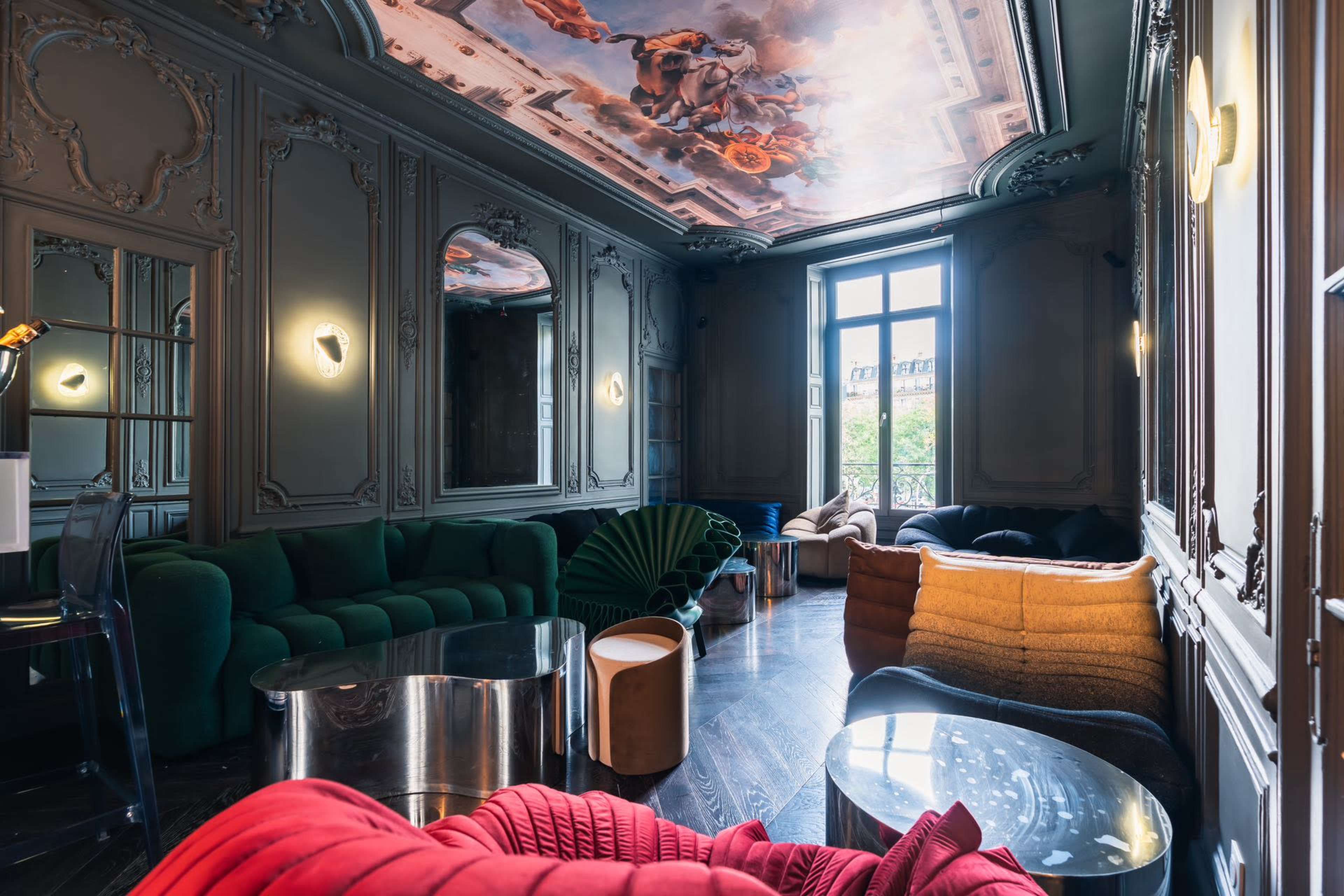 The image shows an elegant interior with decorative walls and a painted ceiling, featuring various modern furniture pieces in different colors and textures.