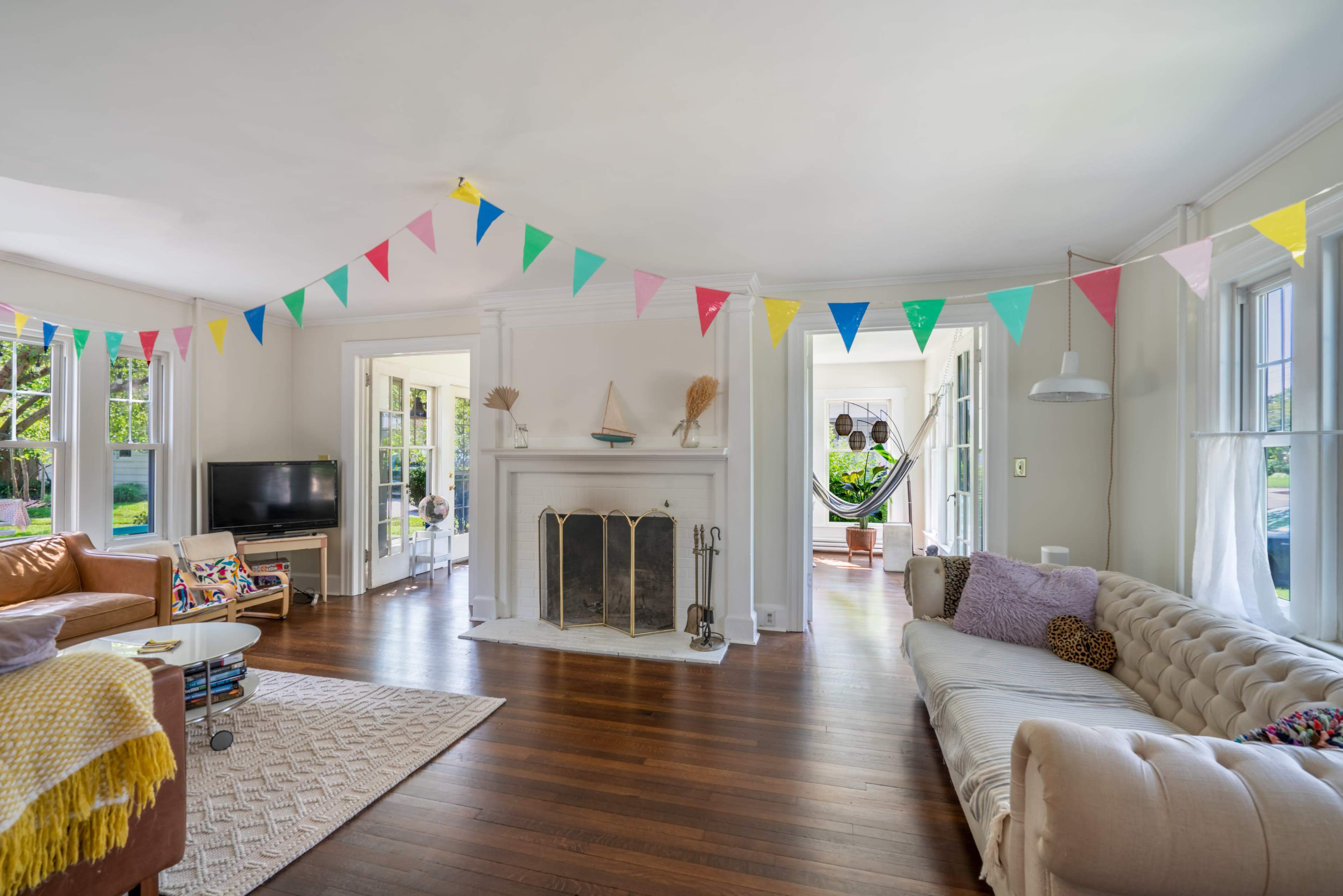 A brightly decorated living room features a fireplace flanked by windows, with colorful bunting strung across the ceiling.