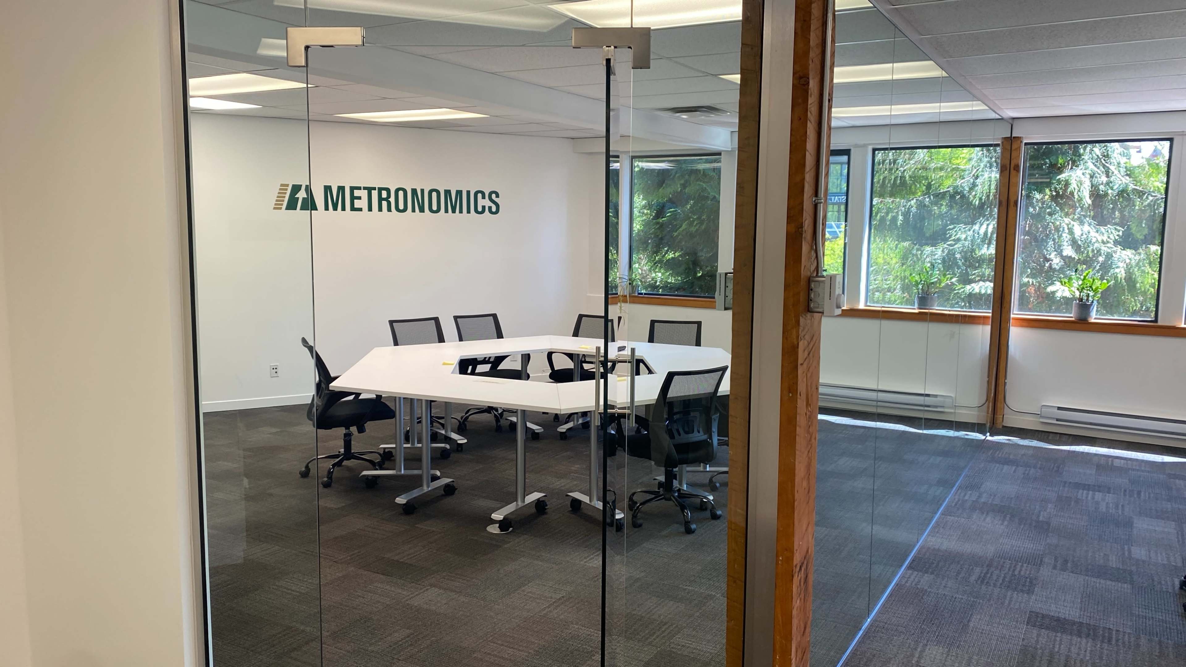 A conference room with a large white table and black chairs is visible through glass doors, featuring the logo of Metronomics on the wall.
