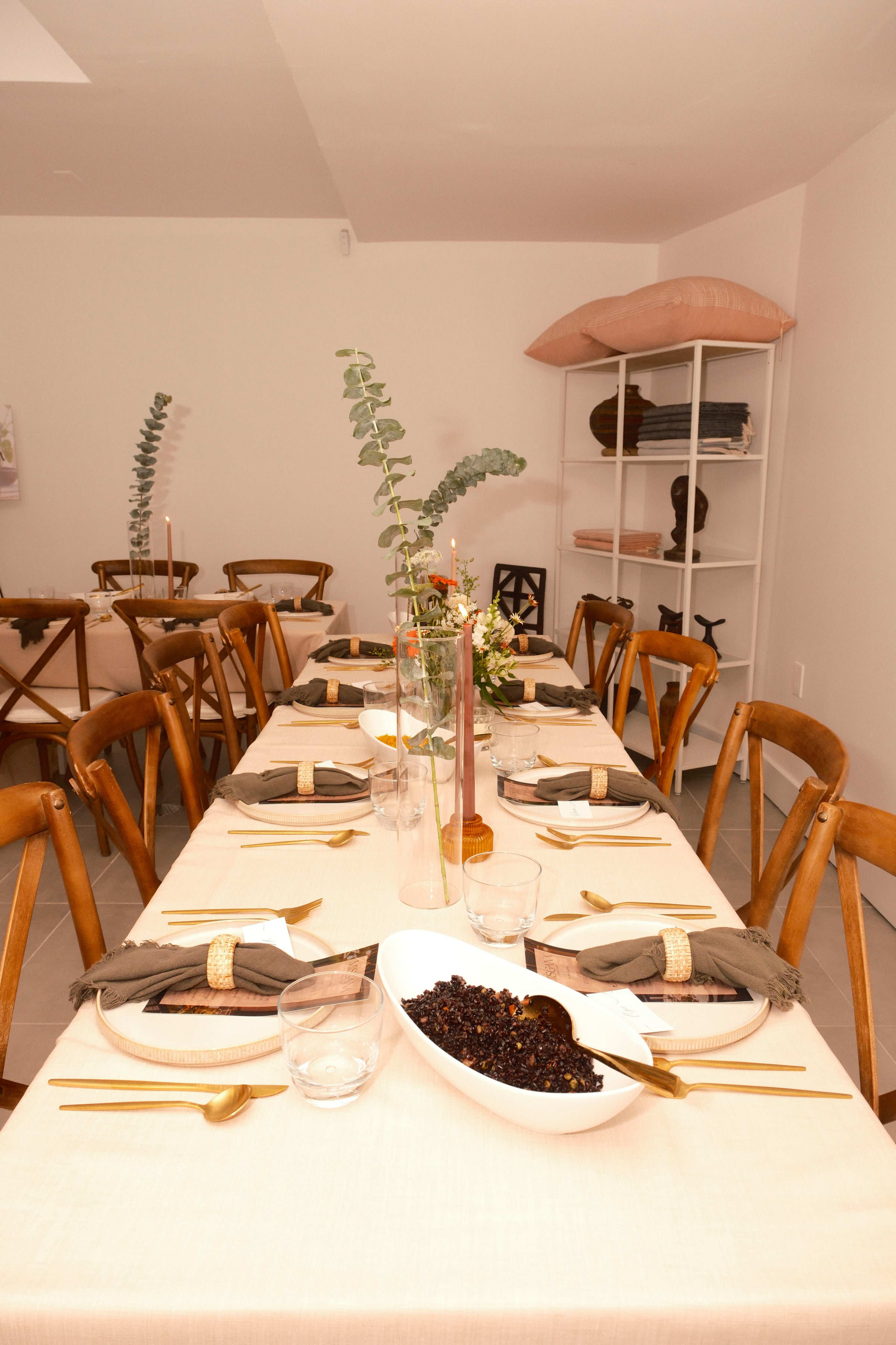 A long dining table is set with beige tablecloths, wooden chairs, and decorative arrangements of greenery and dishes.