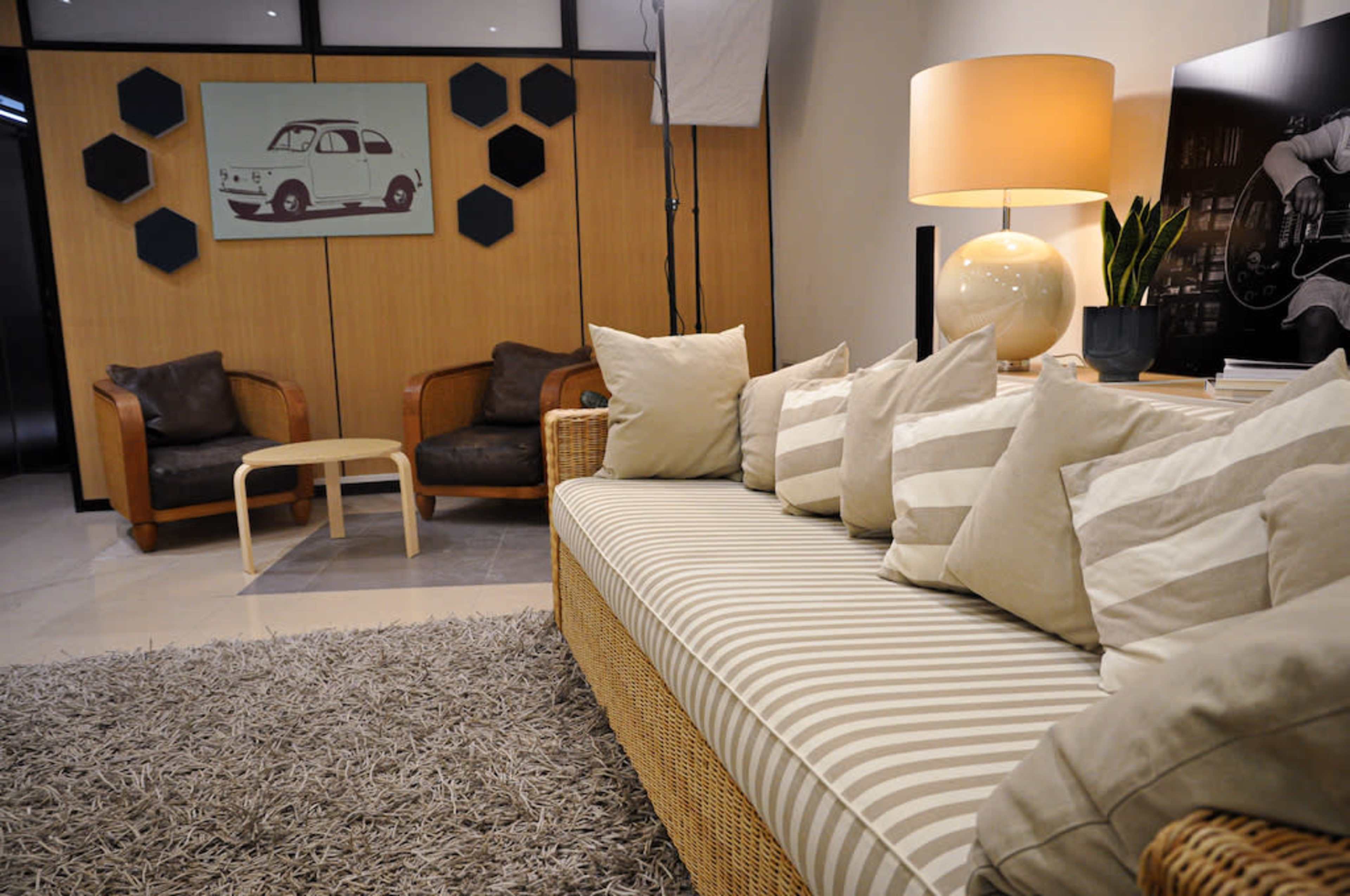 The image shows a modern living room featuring a striped sofa with multiple pillows, a round lamp, a coffee table, and two armchairs against a wooden wall.