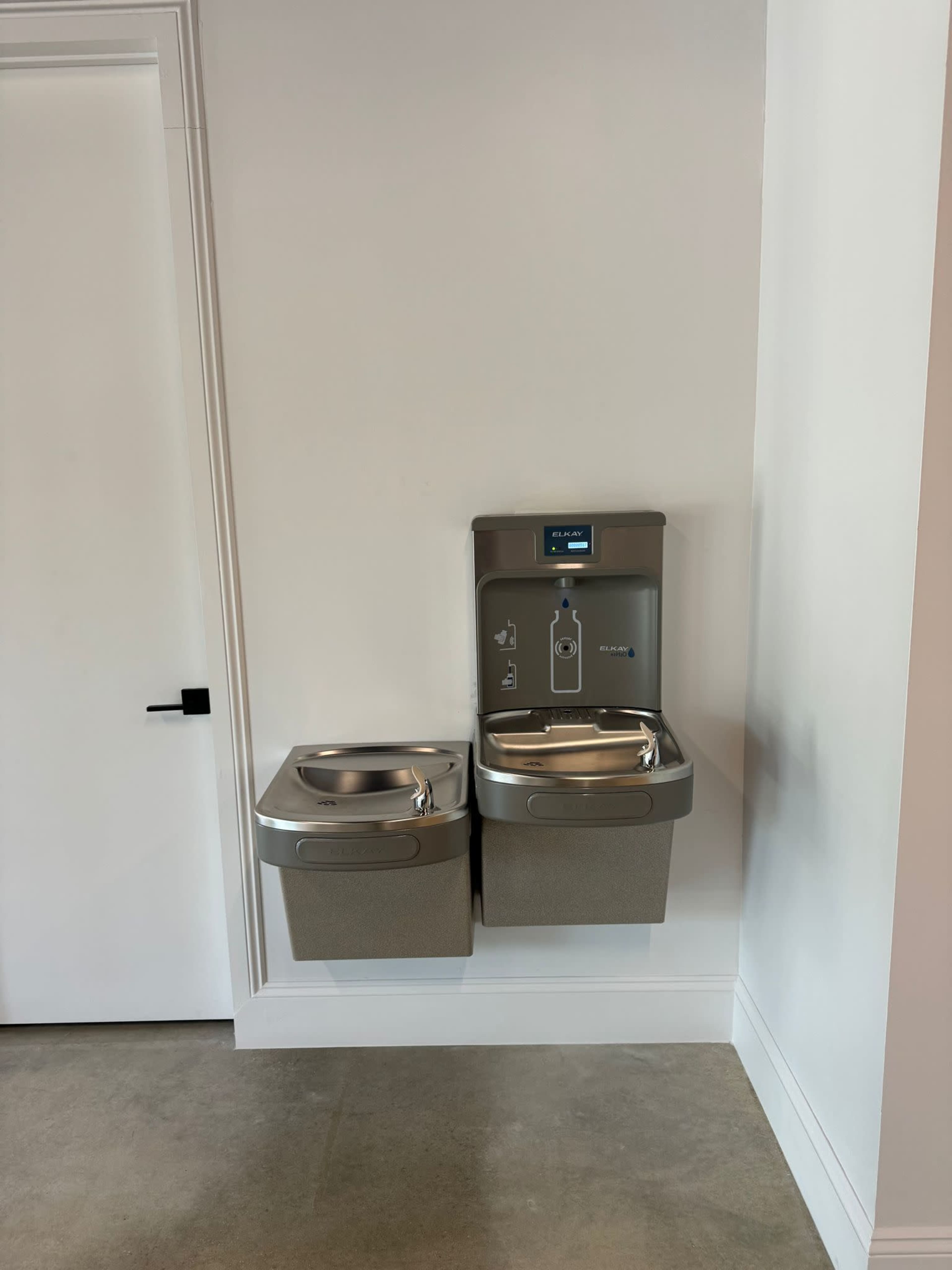 A water fountain with a bottle filling station mounted on a wall beside a standard drinking fountain.