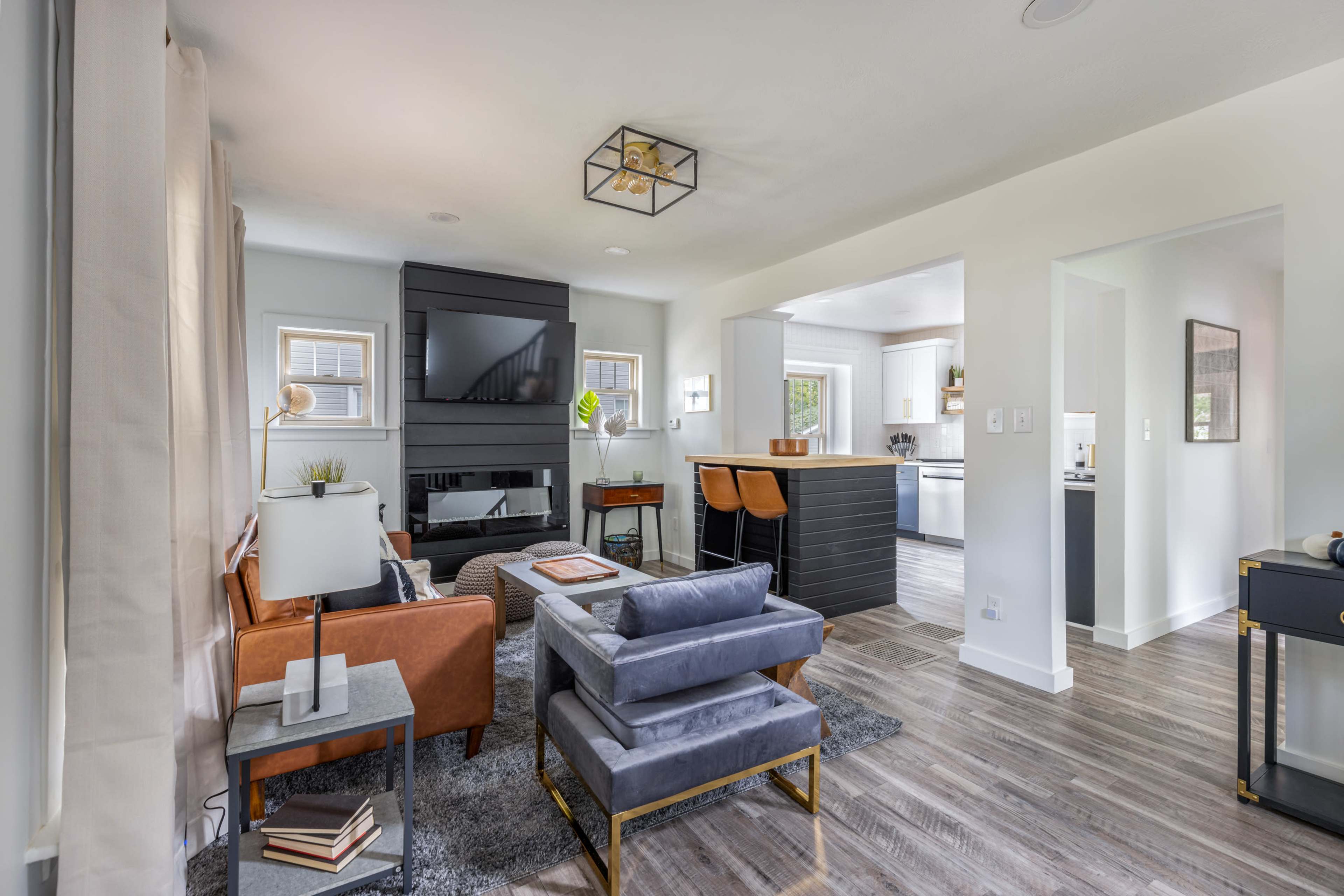 A modern living room with a leather sofa, a gray rug, and a black fireplace, connected to a kitchen area.