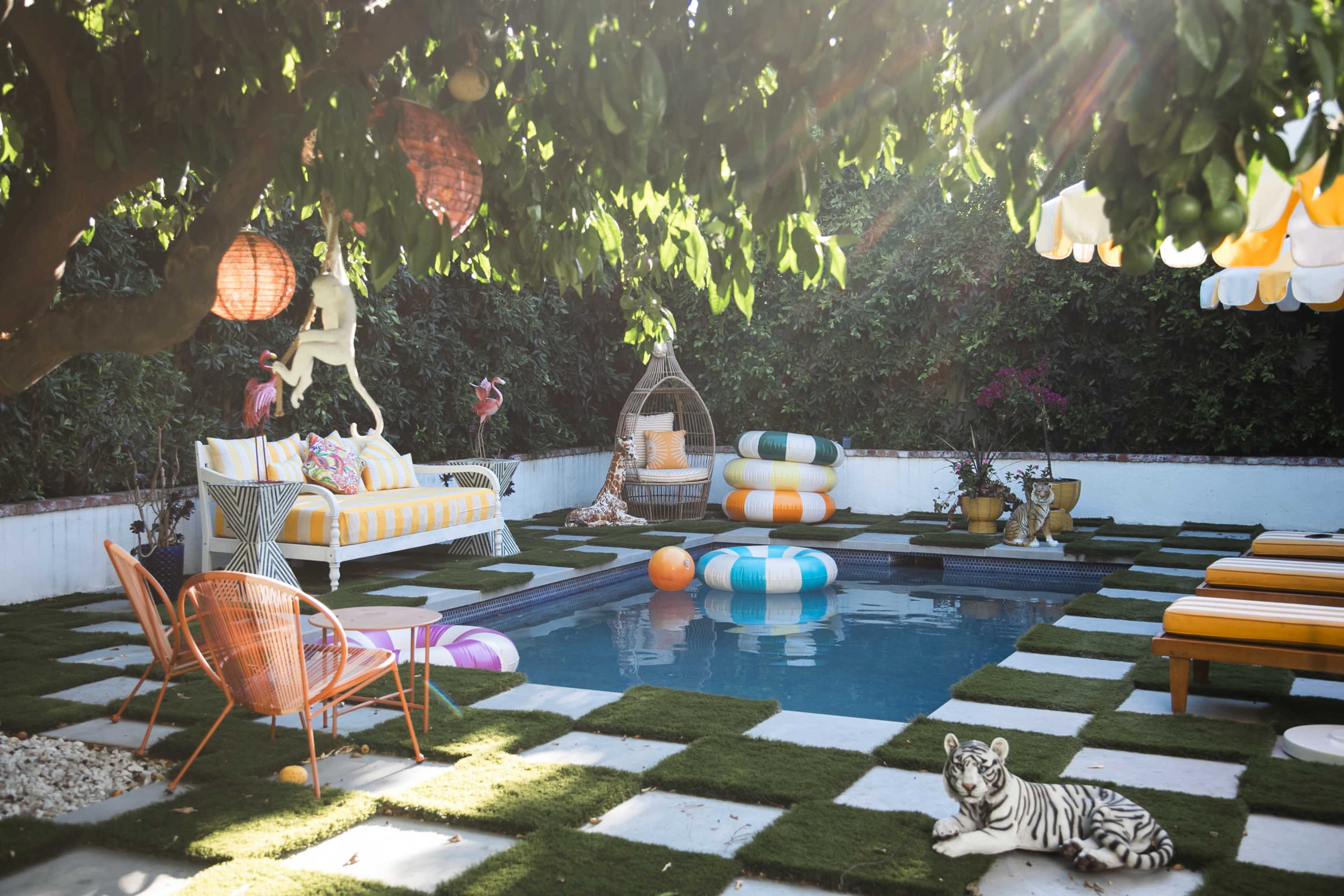 A vibrant outdoor pool area features colorful furniture, decorative cushions, and a playful tiger statue, surrounded by greenery and bright lanterns.