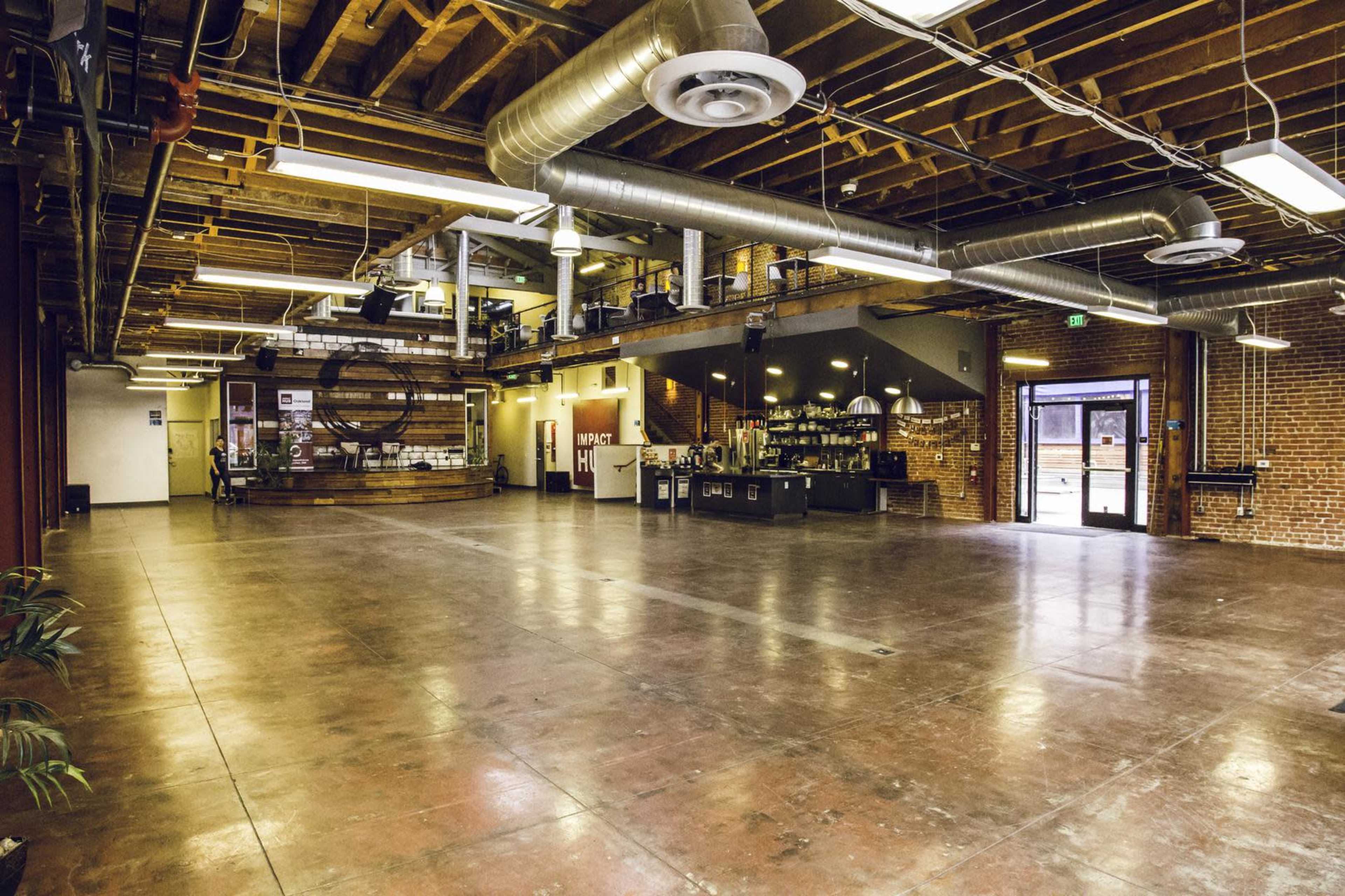 A spacious industrial-style interior with exposed brick walls, large metal ducts, and polished concrete flooring, featuring a kitchenette and seating area.
