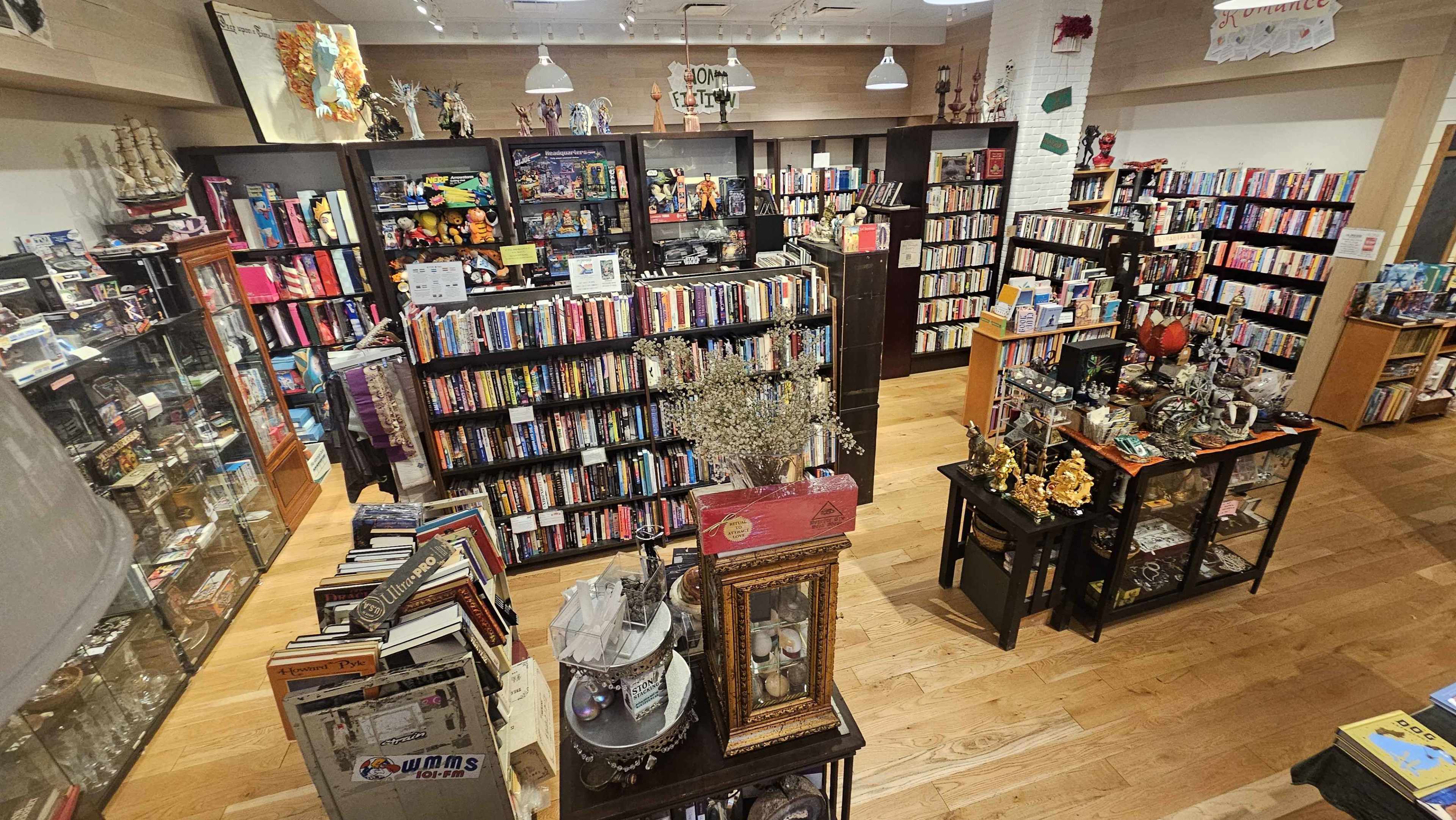 The image shows a cozy bookstore filled with shelves of books and various decorative items arranged on tables throughout the space.