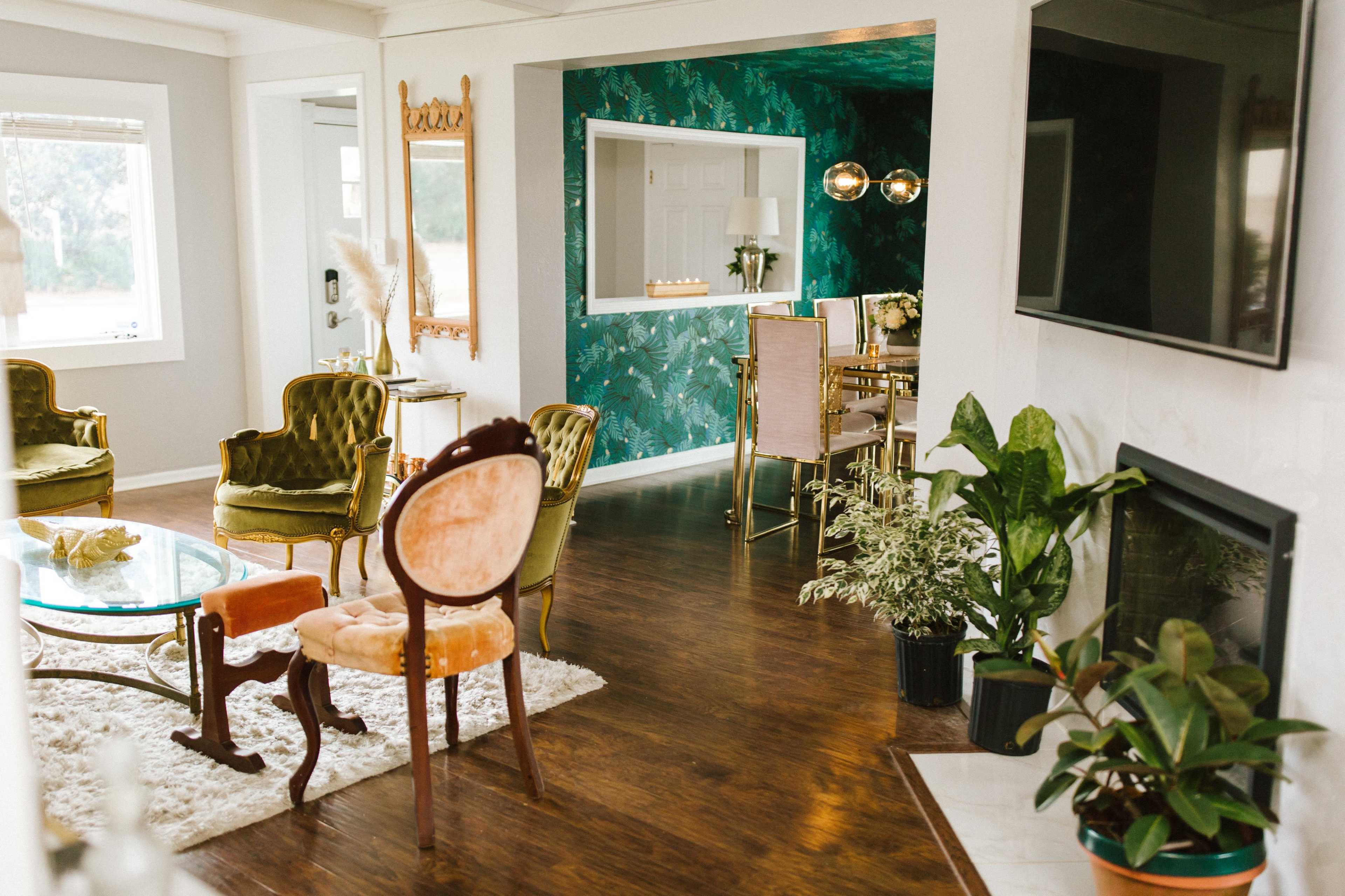 A bright, modern living space with a mix of seating and decorative elements, featuring a green accent wall and a dining area visible in the background.