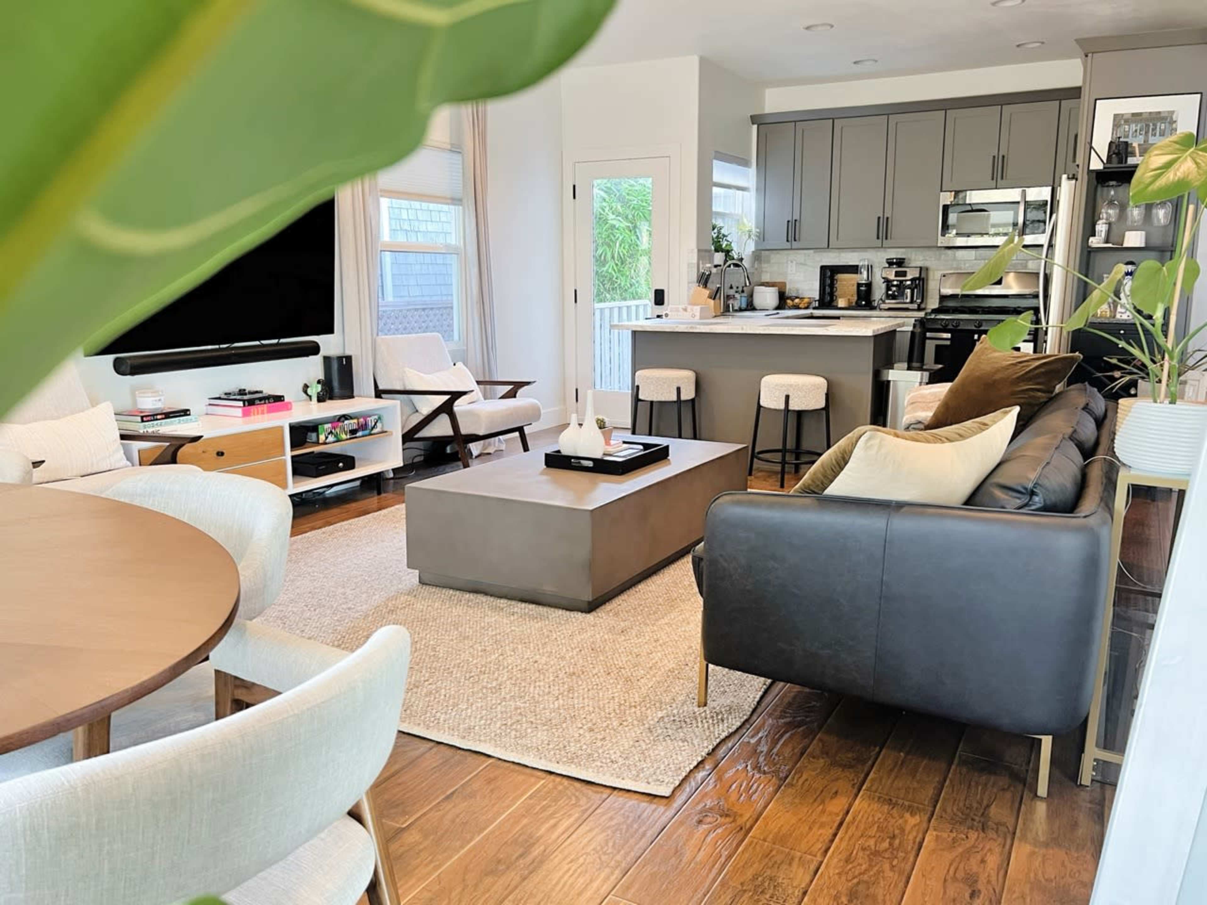 A modern living room with a sectional sofa, a coffee table, and a dining area, featuring a kitchen in the background.