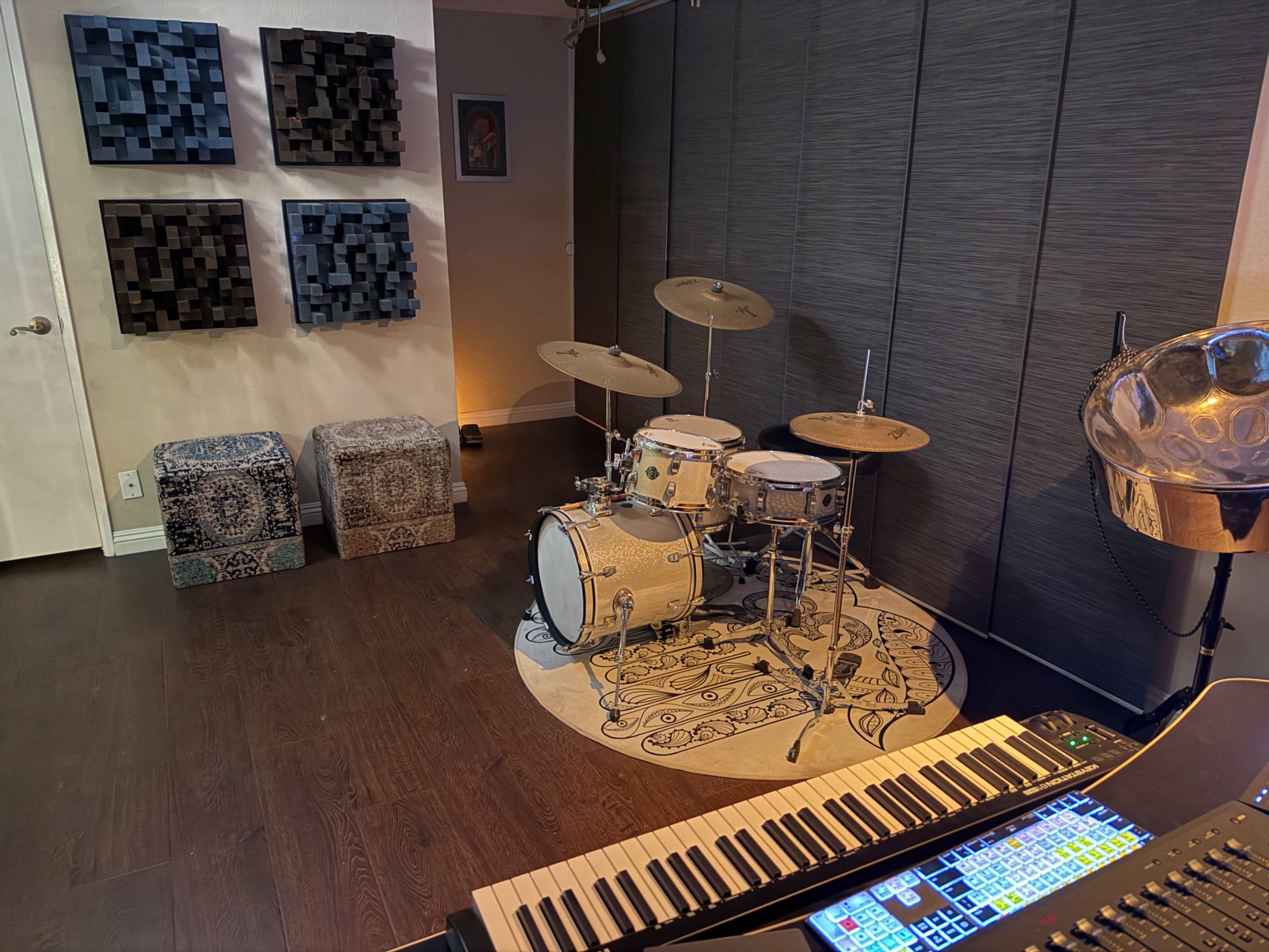 The image shows a music studio with a drum set, a keyboard, and wall-mounted acoustic panels.