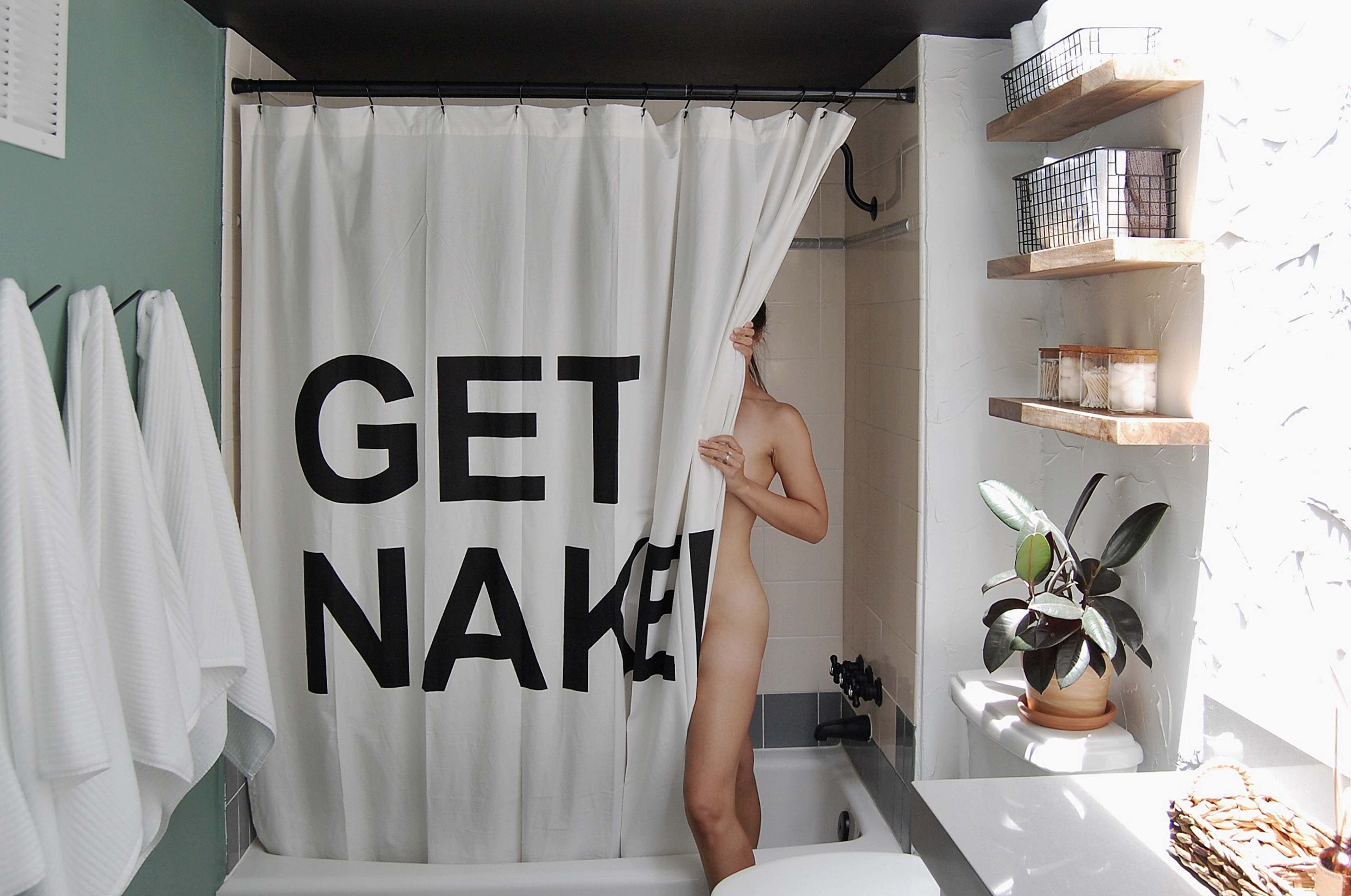 A person partially steps out from behind a shower curtain with large text that reads "GET NAKED" in a bathroom setting.