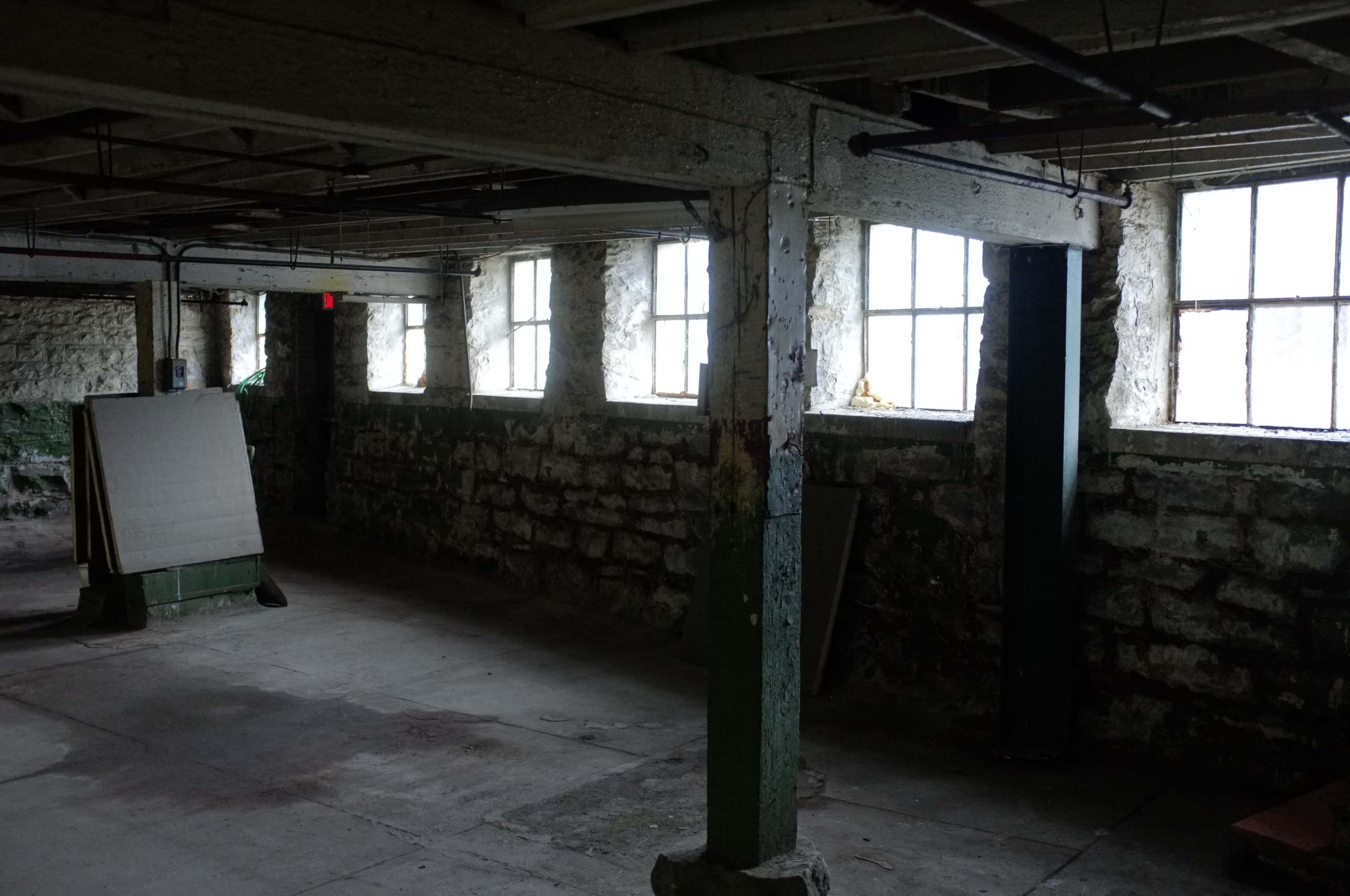 A dimly lit basement with stone walls, large windows, and a few wooden beams.
