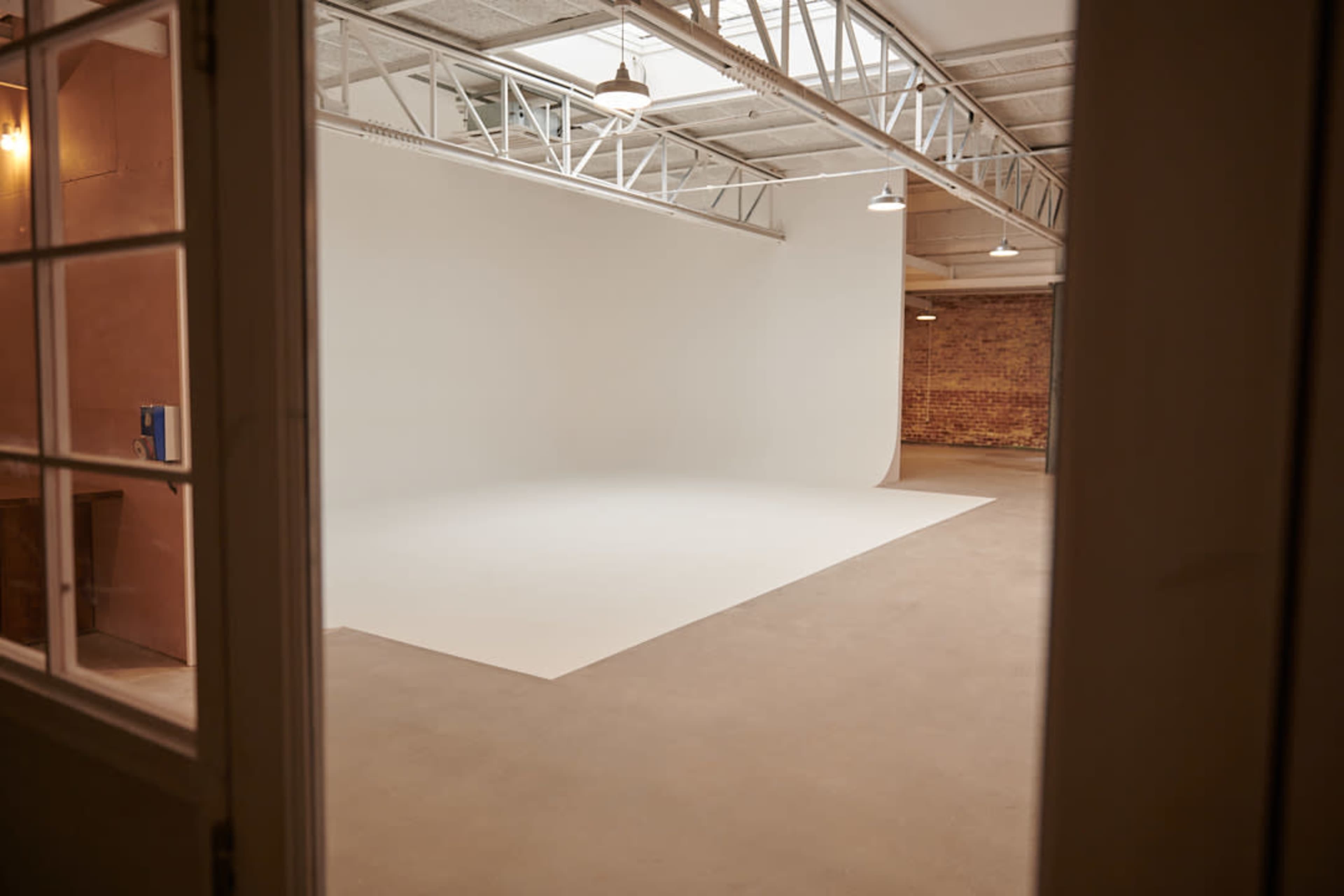 A spacious photography studio features a large white backdrop and concrete flooring with exposed beams overhead.