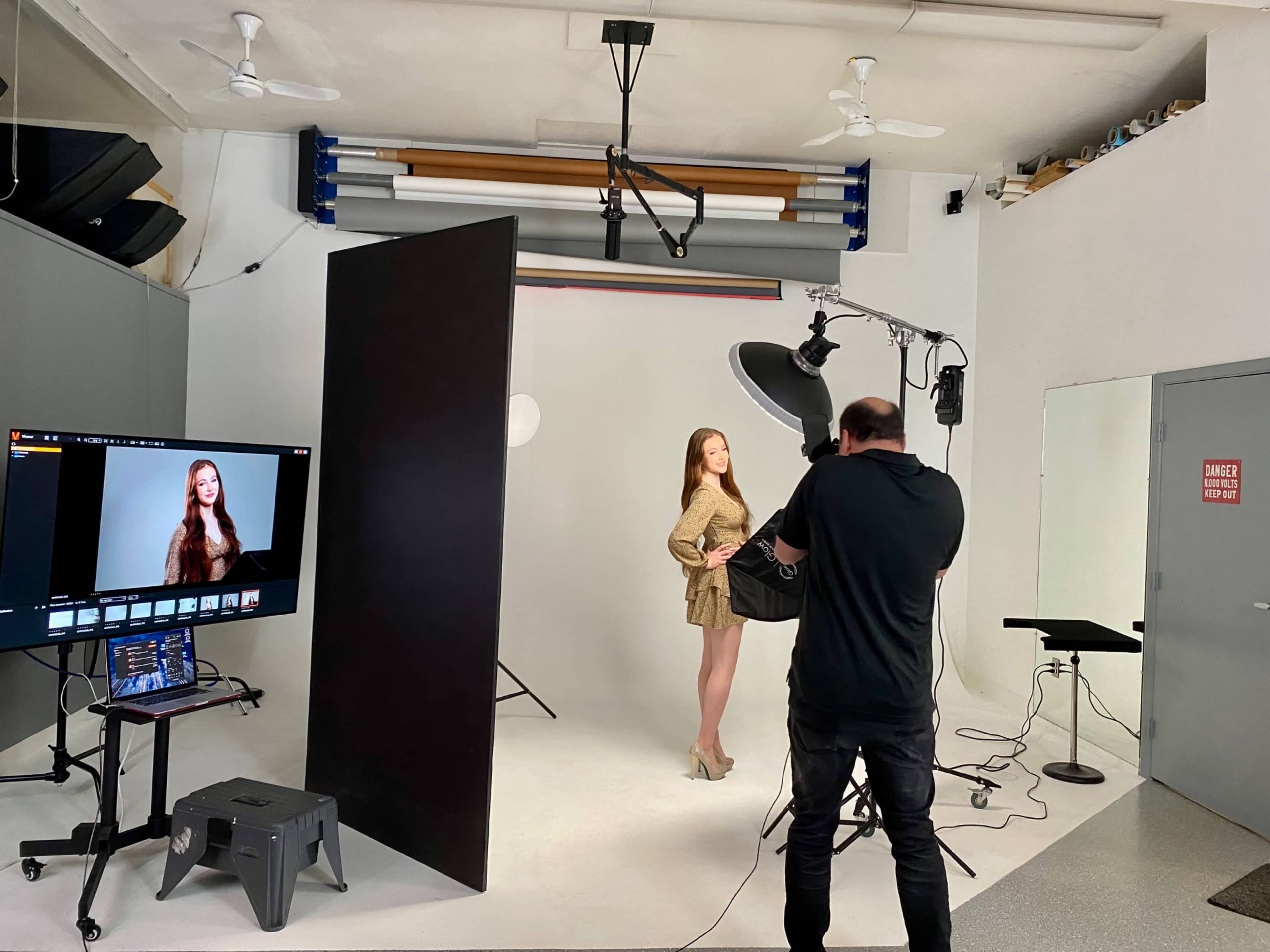 A photographer captures a model posing in a studio setup with backdrop and lighting equipment.