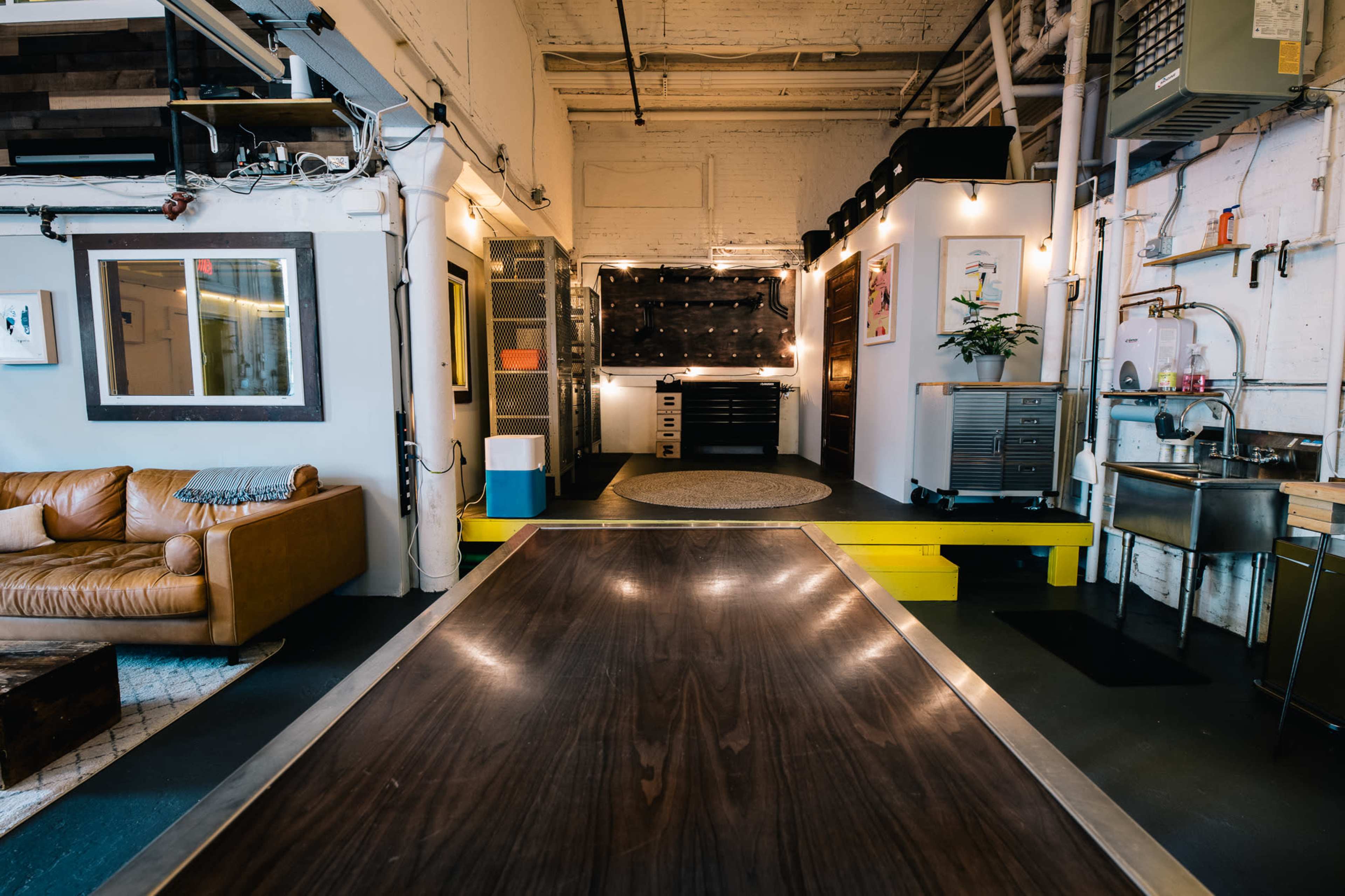 A modern interior space featuring a leather sofa, a long wooden table, and a kitchenette area with metal appliances.
