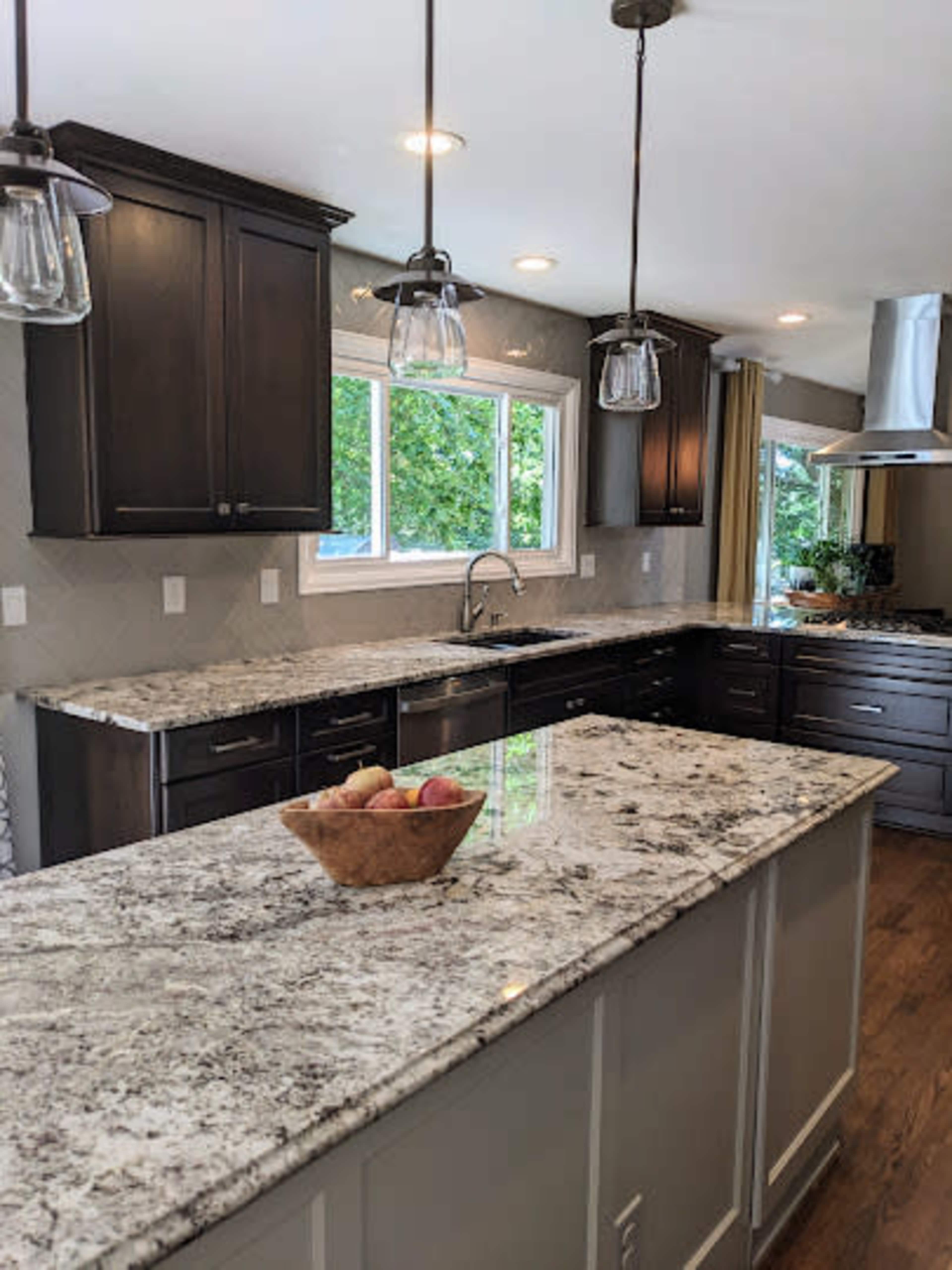 The kitchen features dark cabinets, a granite countertop, and pendant lighting above a center island with a fruit bowl.