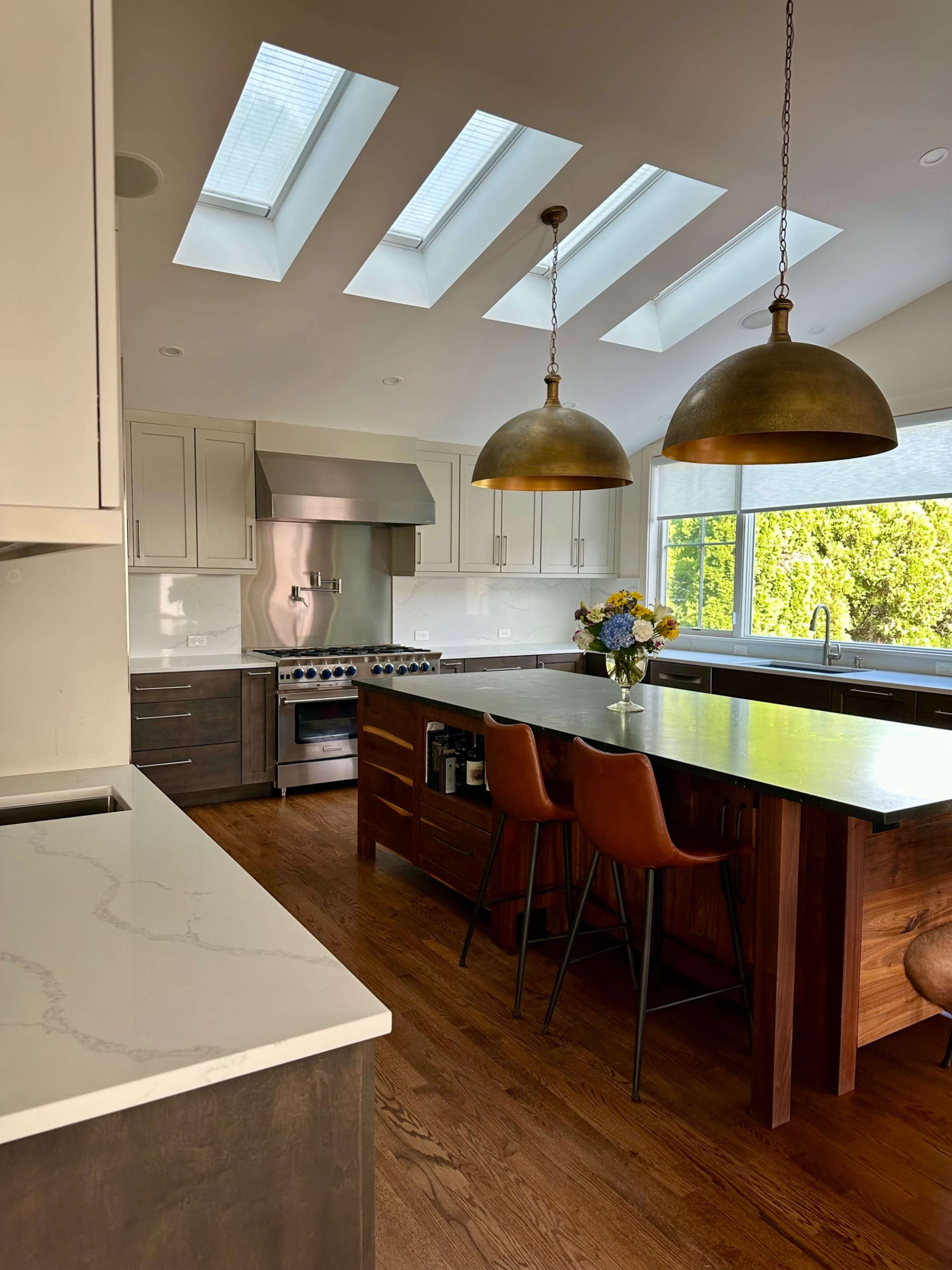 The kitchen features modern appliances, a large island with seating, and skylights that provide natural light.