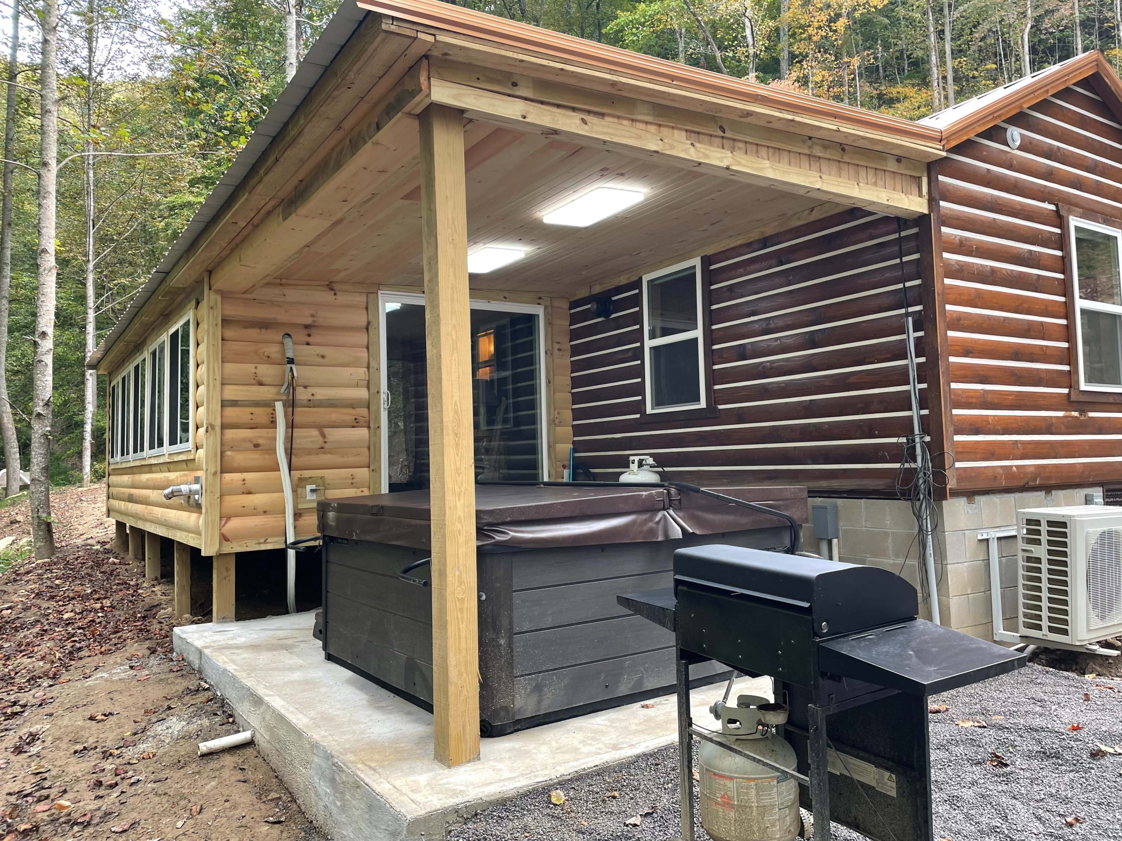 A cabin with a wooden exterior, featuring a covered porch area that includes a hot tub and a grill.