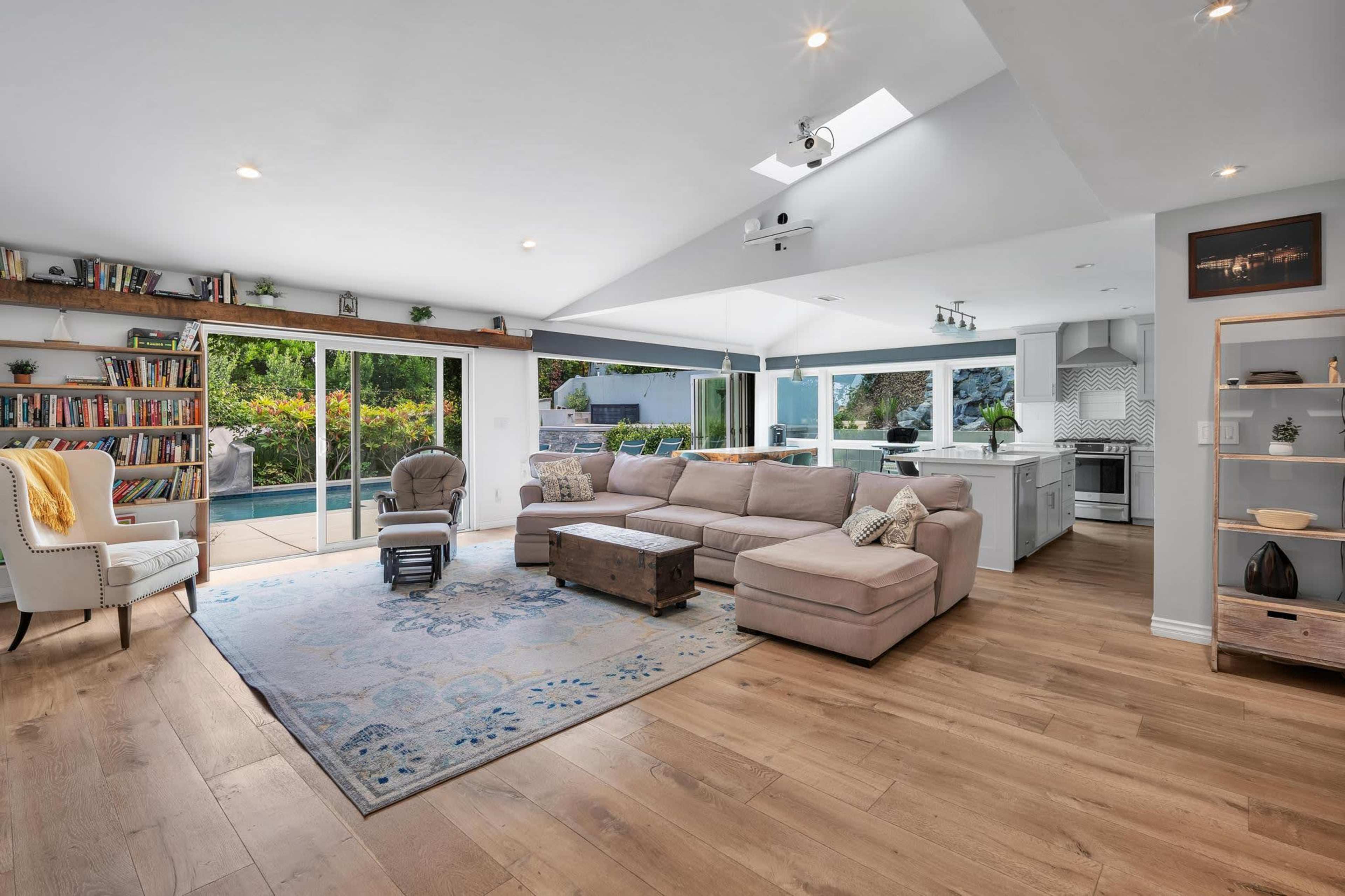 A modern living room features a large sectional sofa, a coffee table, bookshelves, and sliding glass doors that open to an outdoor patio.