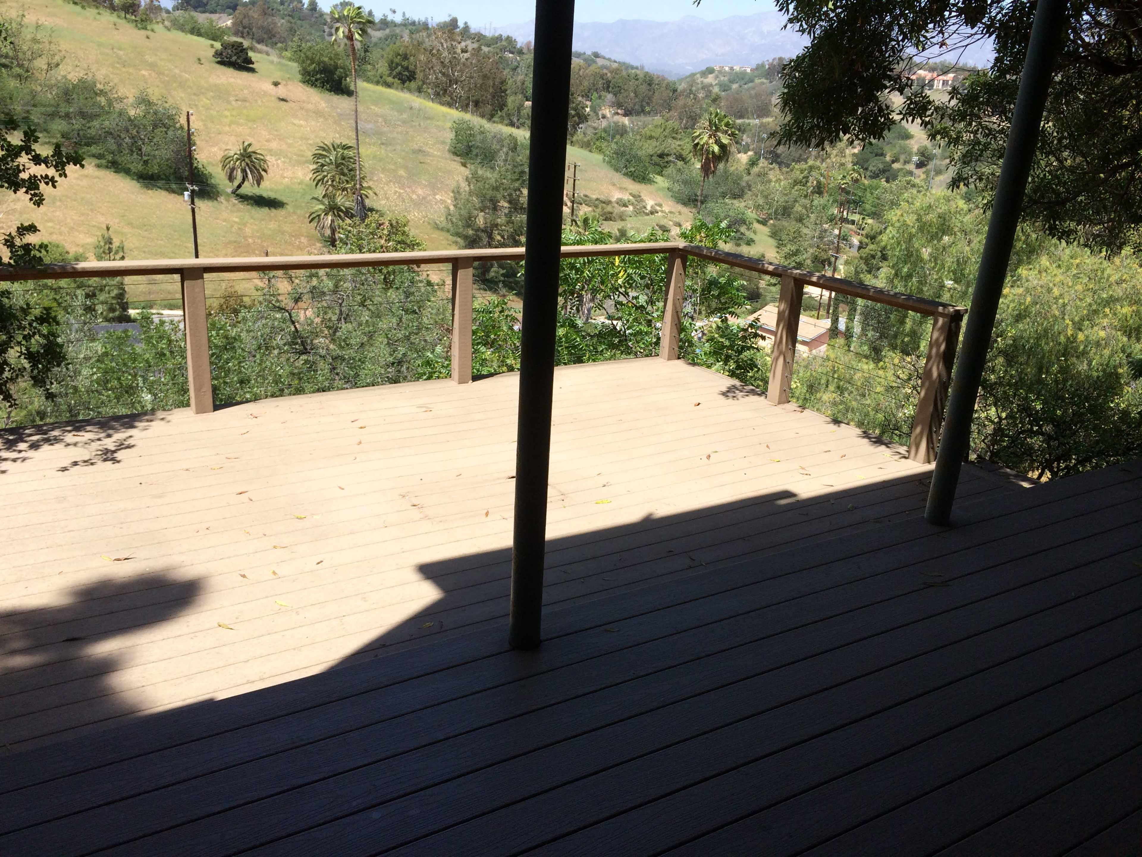 The image shows a wooden deck with a railing overlooking a grassy hillside and trees.