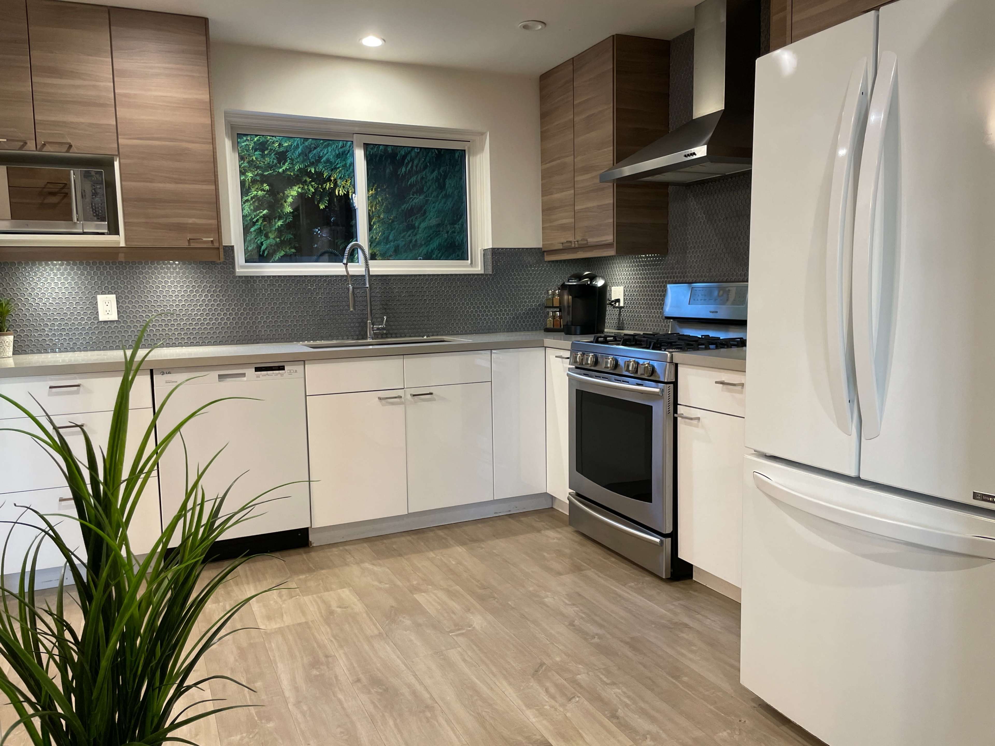 A modern kitchen featuring light wood cabinetry, stainless steel appliances, and a window overlooking greenery.