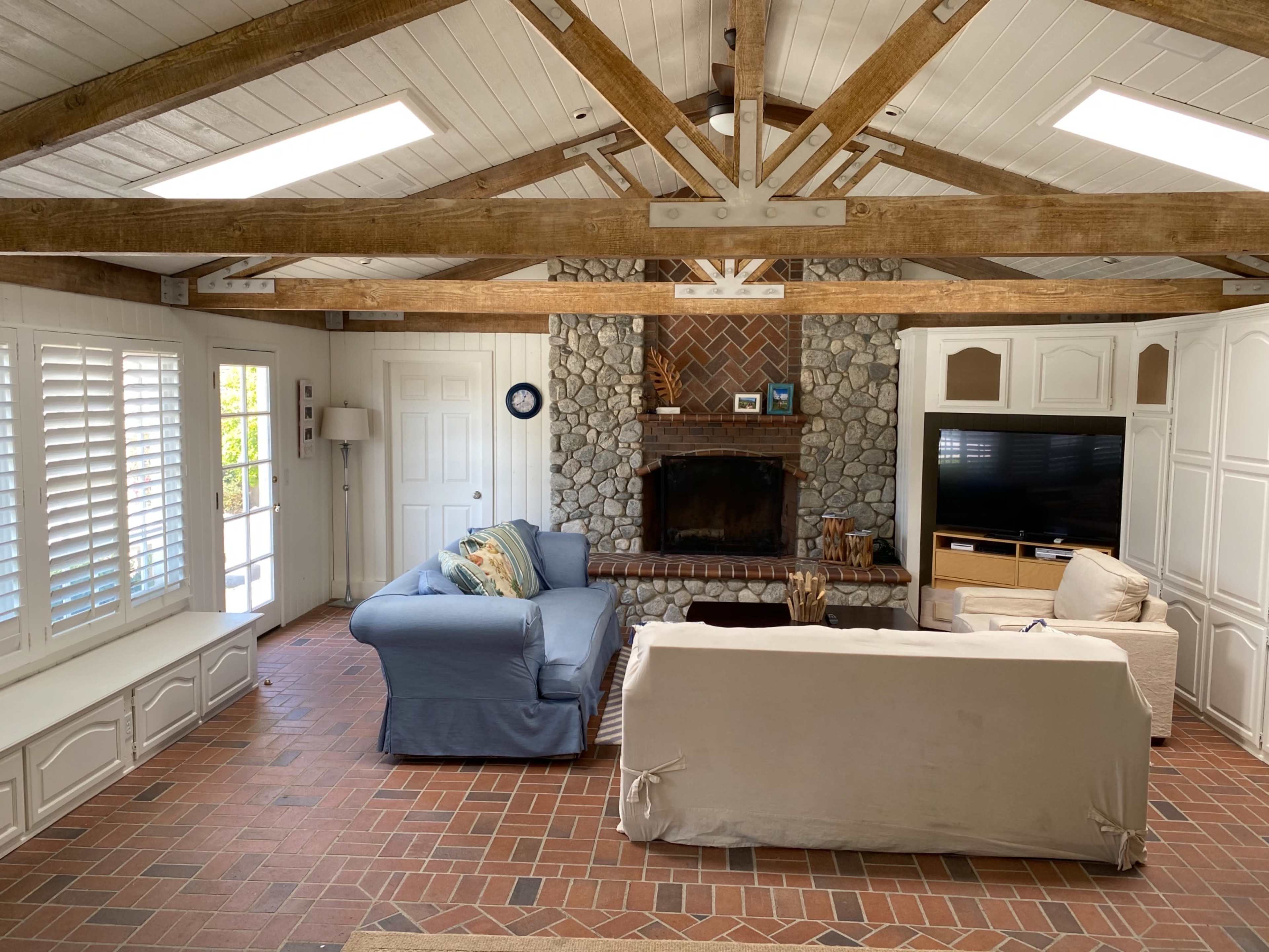 A living room with a stone fireplace, exposed wooden beams, and two sofas facing each other.