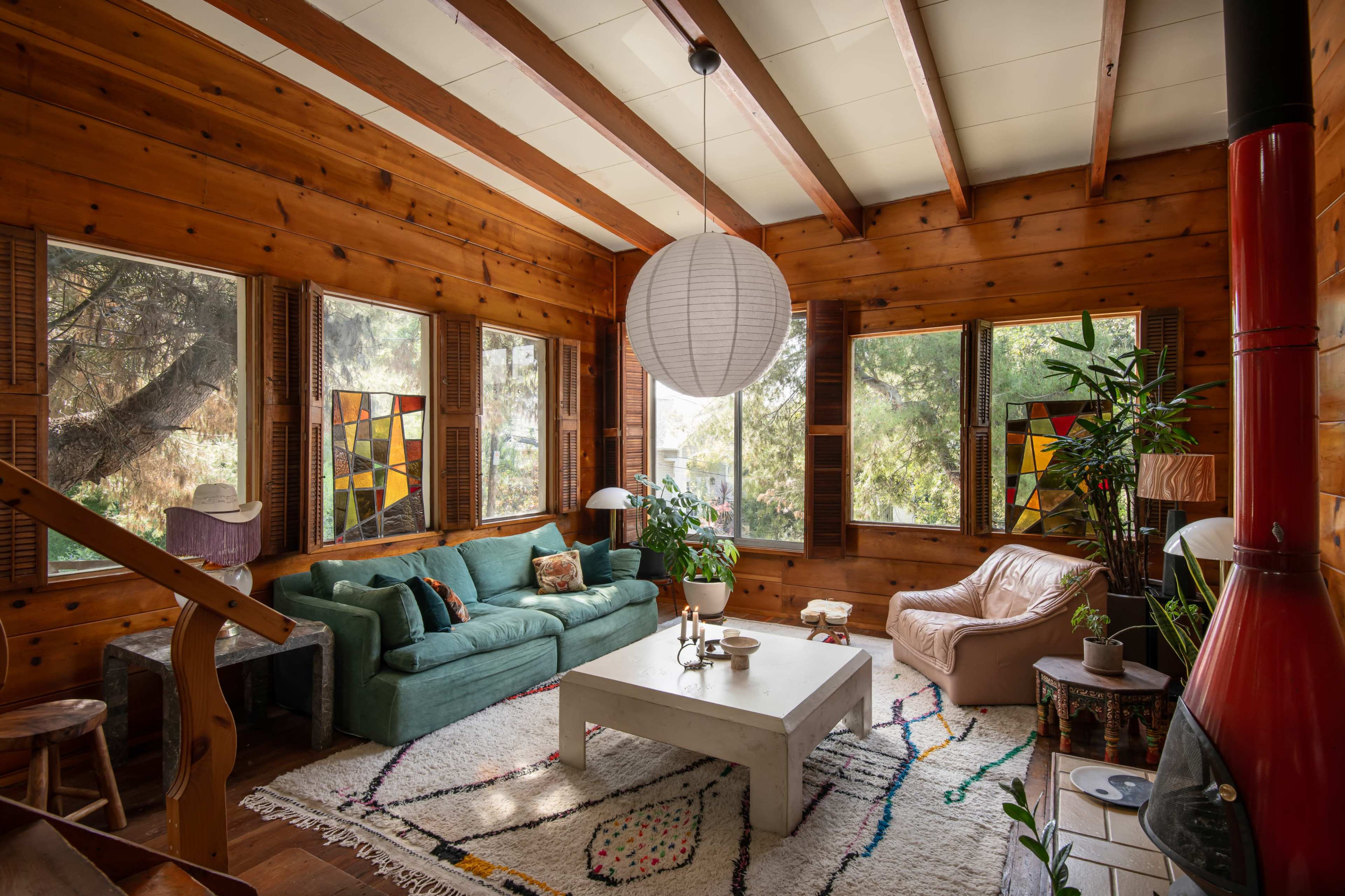 A wooden-paneled living room featuring a green sofa, a white coffee table, and large windows with colorful stained glass.