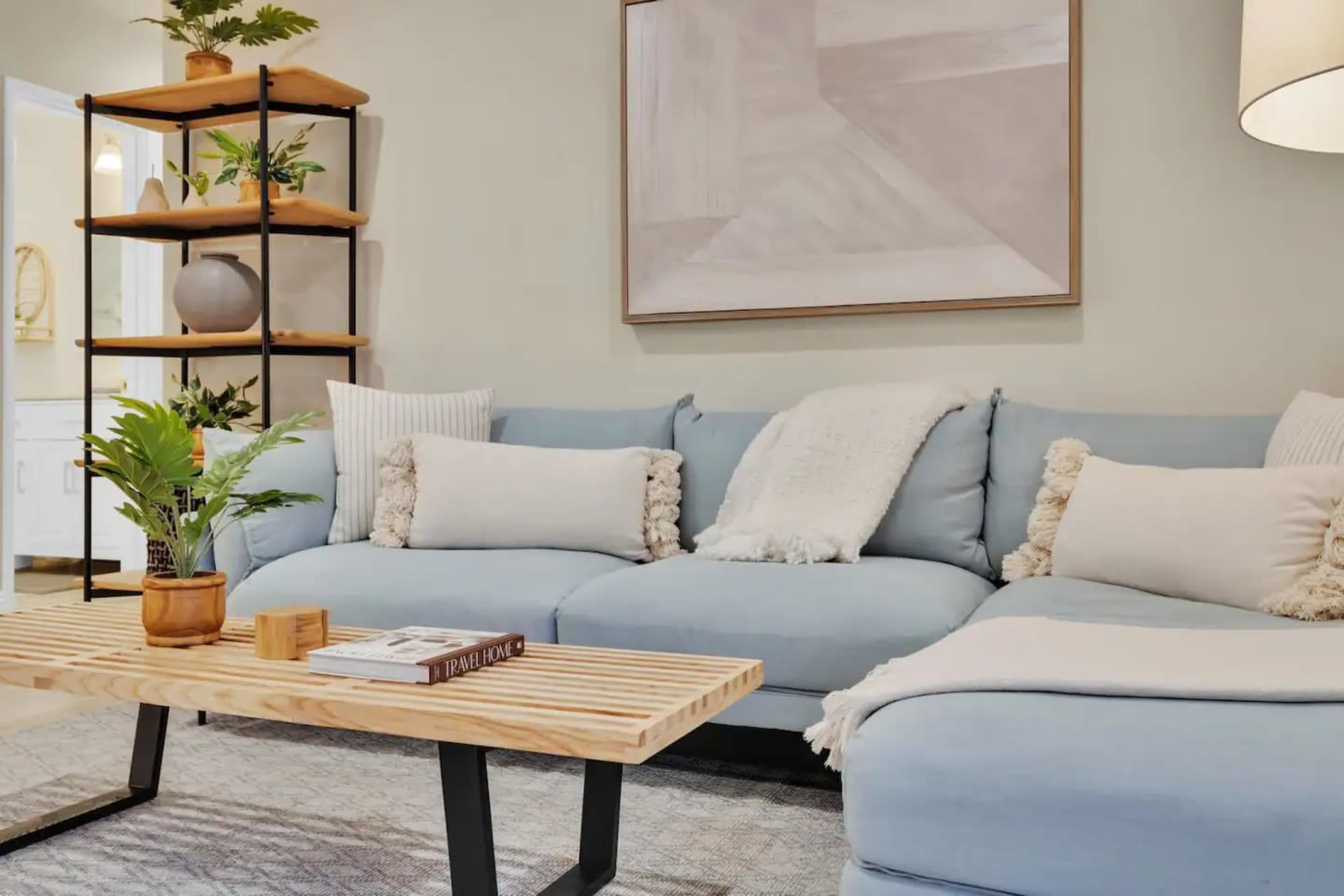 A light blue sectional sofa with decorative pillows, a wooden coffee table, and a plant on a shelf in a well-lit living room.