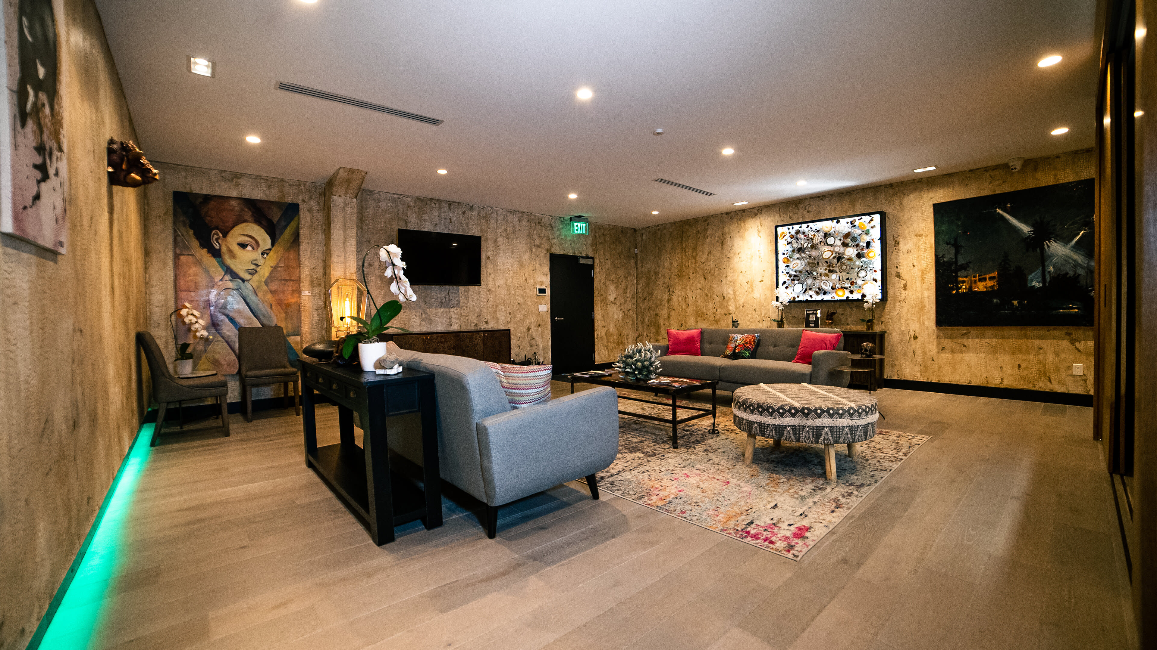 A modern lounge area features gray sofas, a round ottoman, and art pieces on the walls.