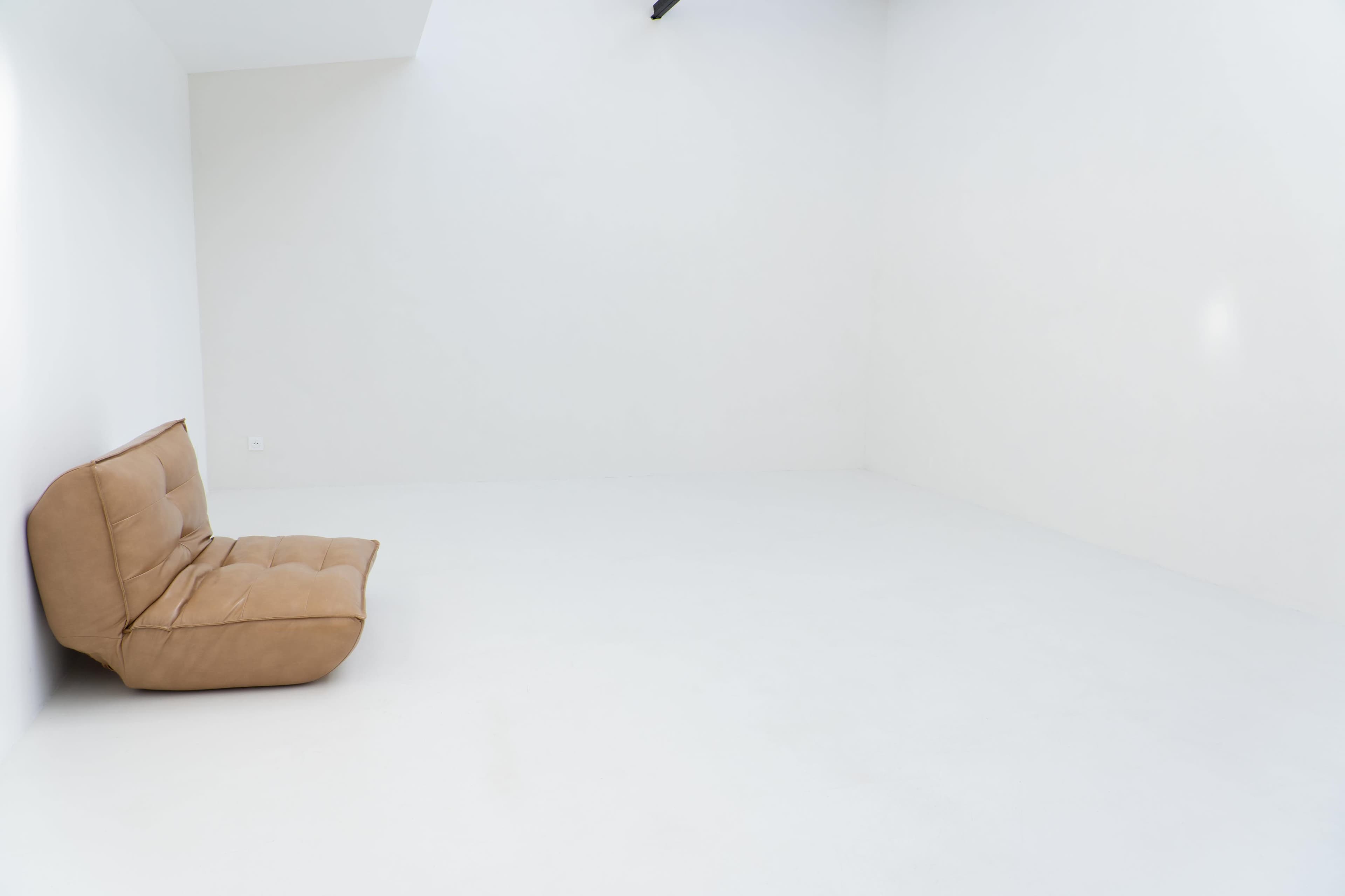 A brown, cushioned sofa is positioned in an empty, white-walled room with a smooth floor.