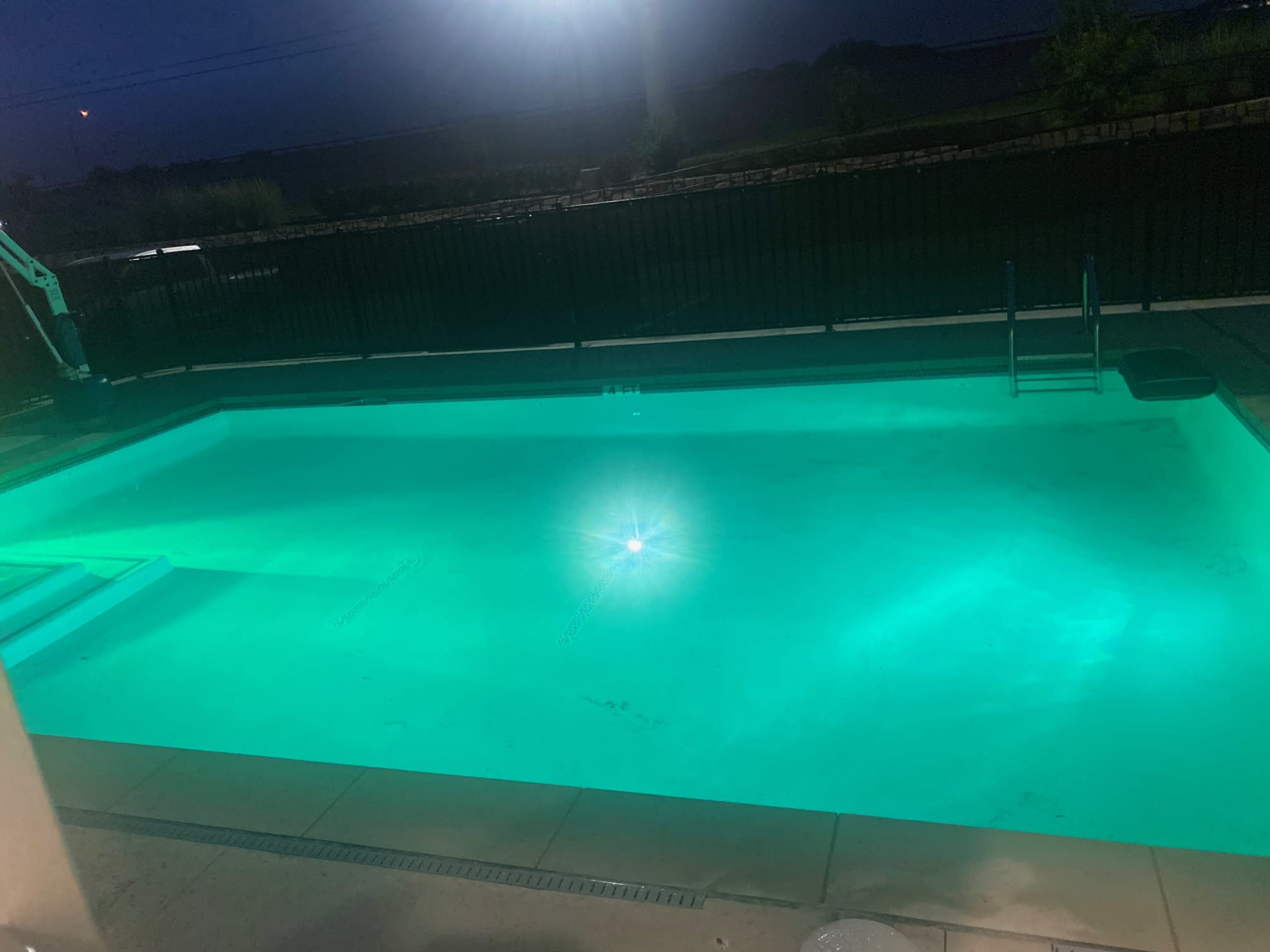 A well-lit swimming pool glows turquoise under the night sky.