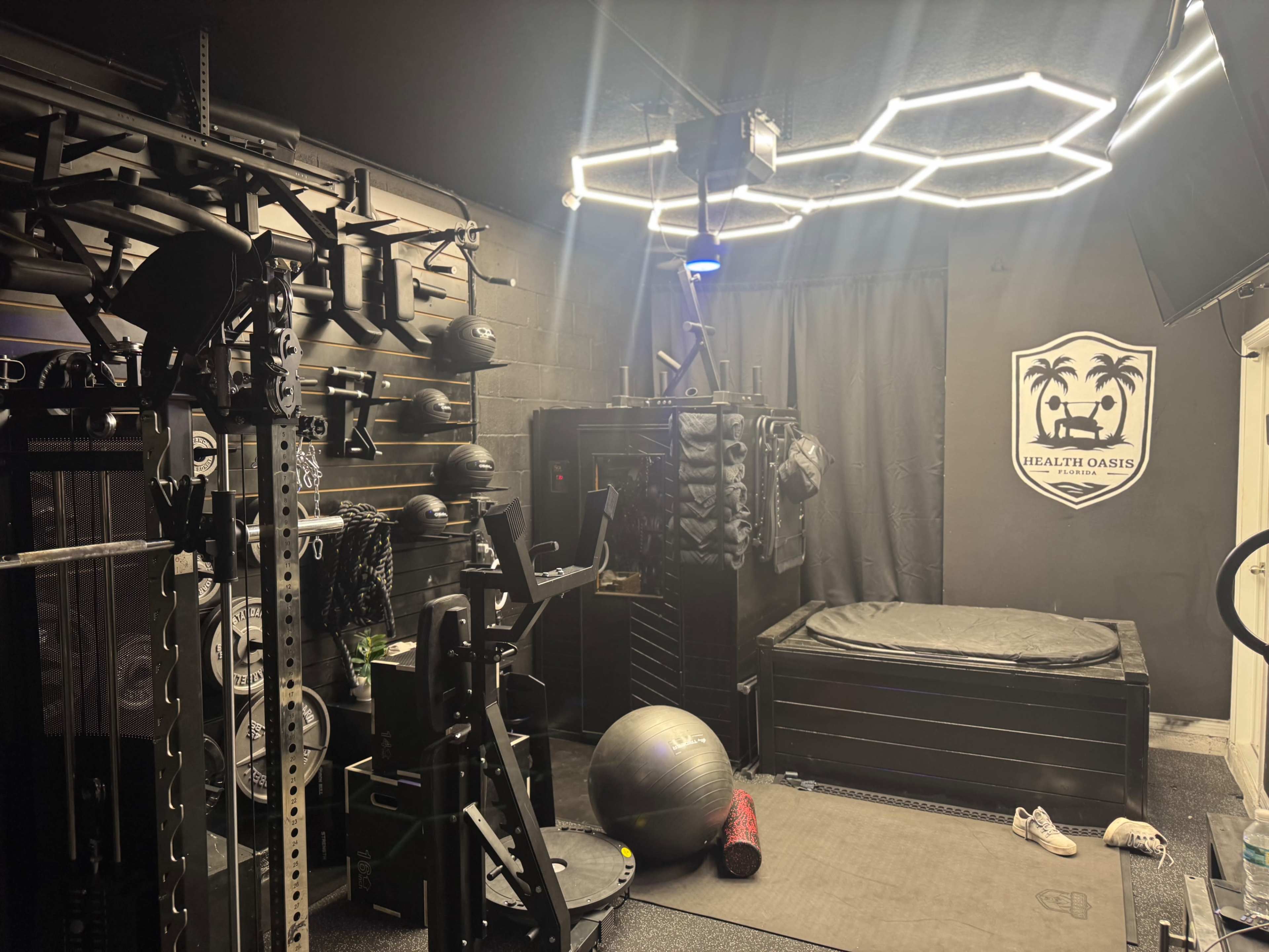 The image shows a home gym equipped with various exercise equipment, including weights, fitness balls, and a large padded area.