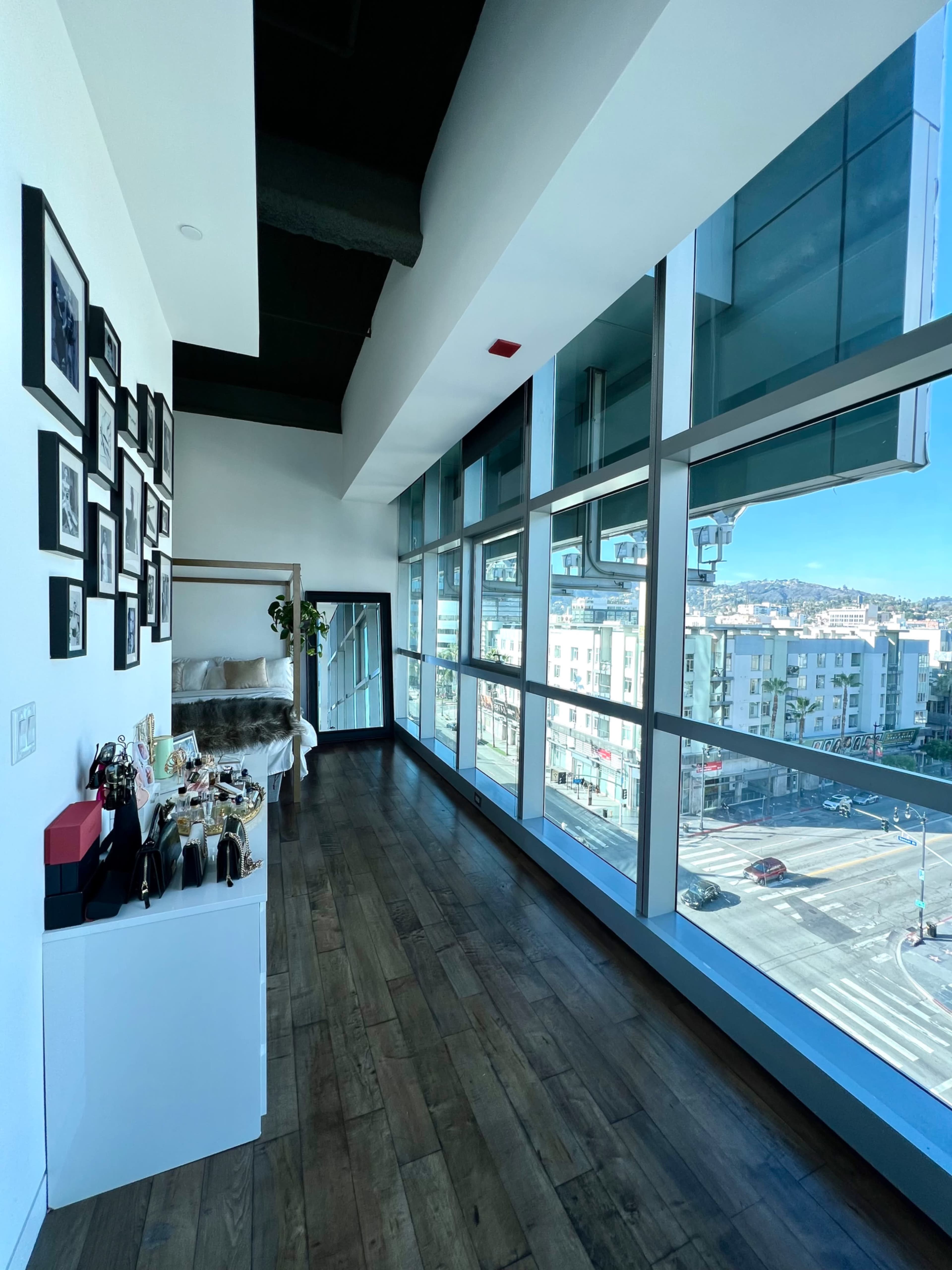 A modern interior features large windows with a view of a busy intersection, complemented by a gallery wall of framed photos.