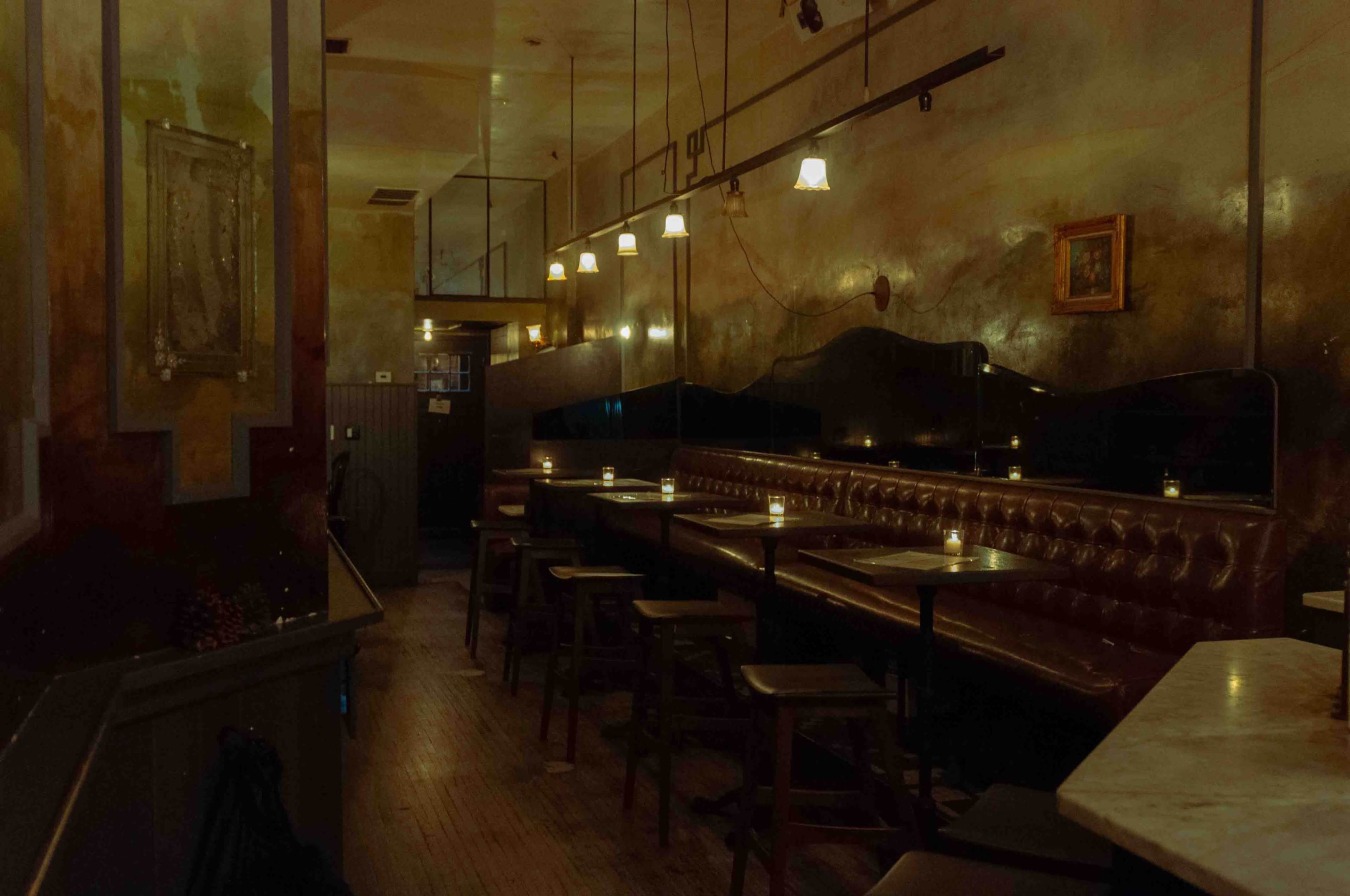 The image shows a dimly lit restaurant interior with leather seating, small tables, and candles on each table.