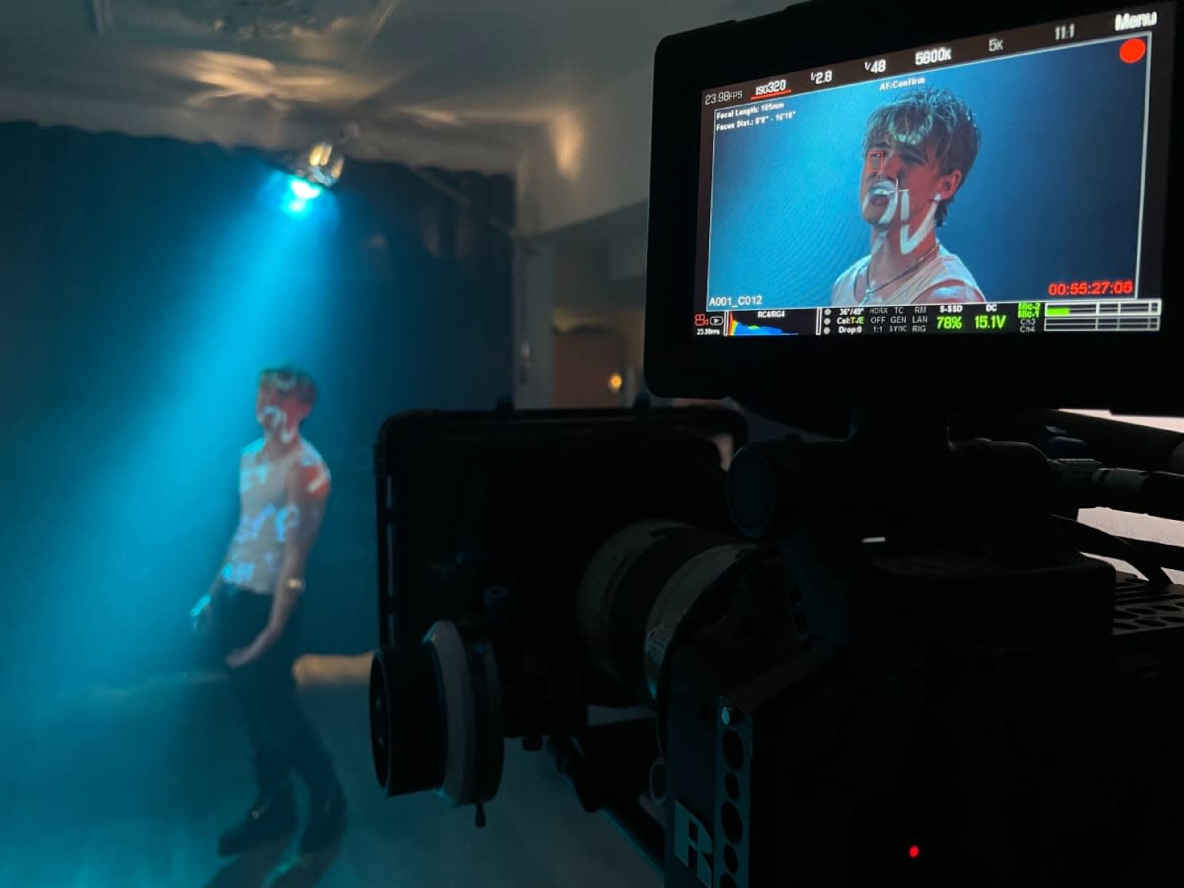 A camera is focused on a person standing under a spotlight in a dimly lit room.