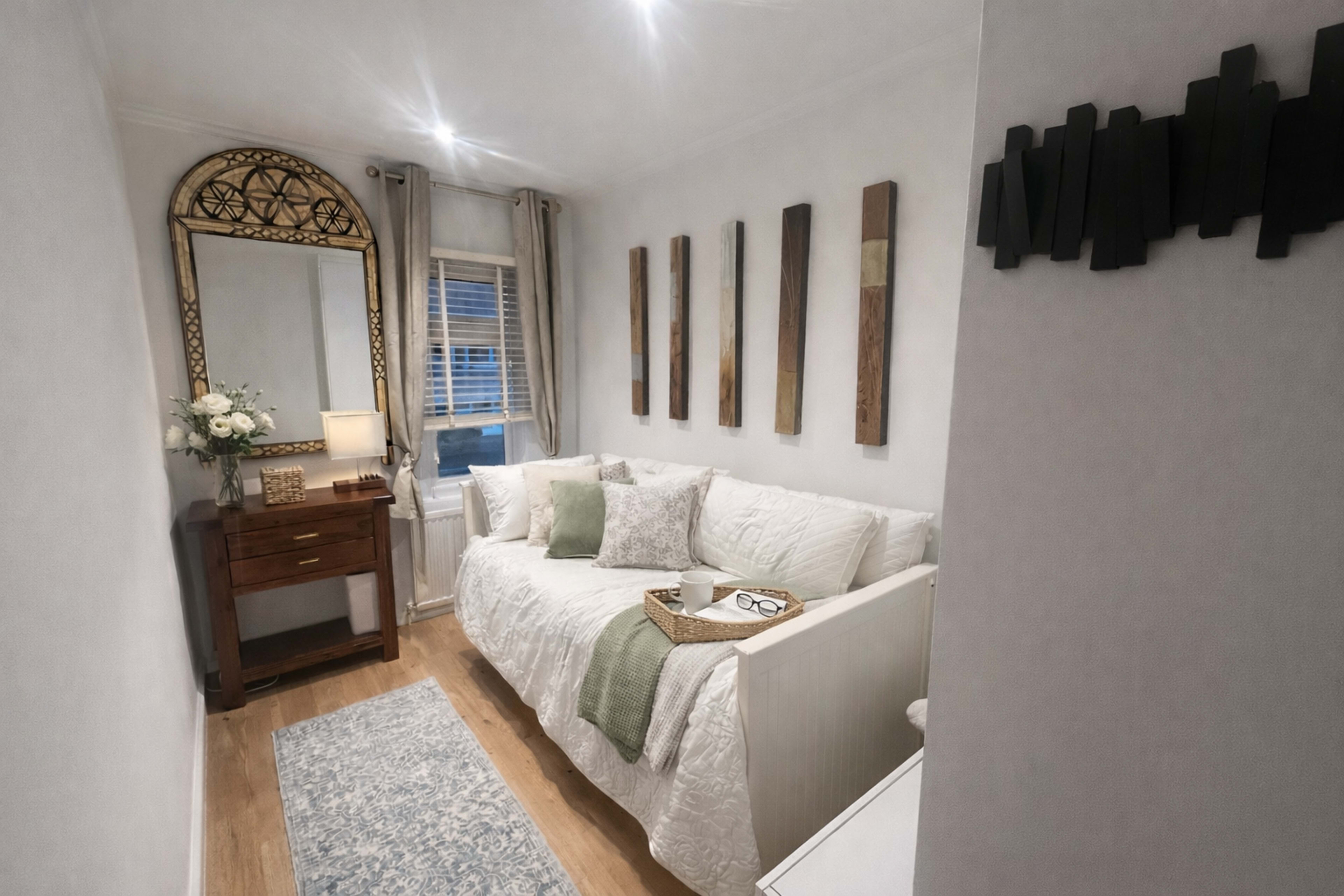 The image shows a cozy living room with a white sofa, a wooden table, a large mirror, and several decorative wall panels.