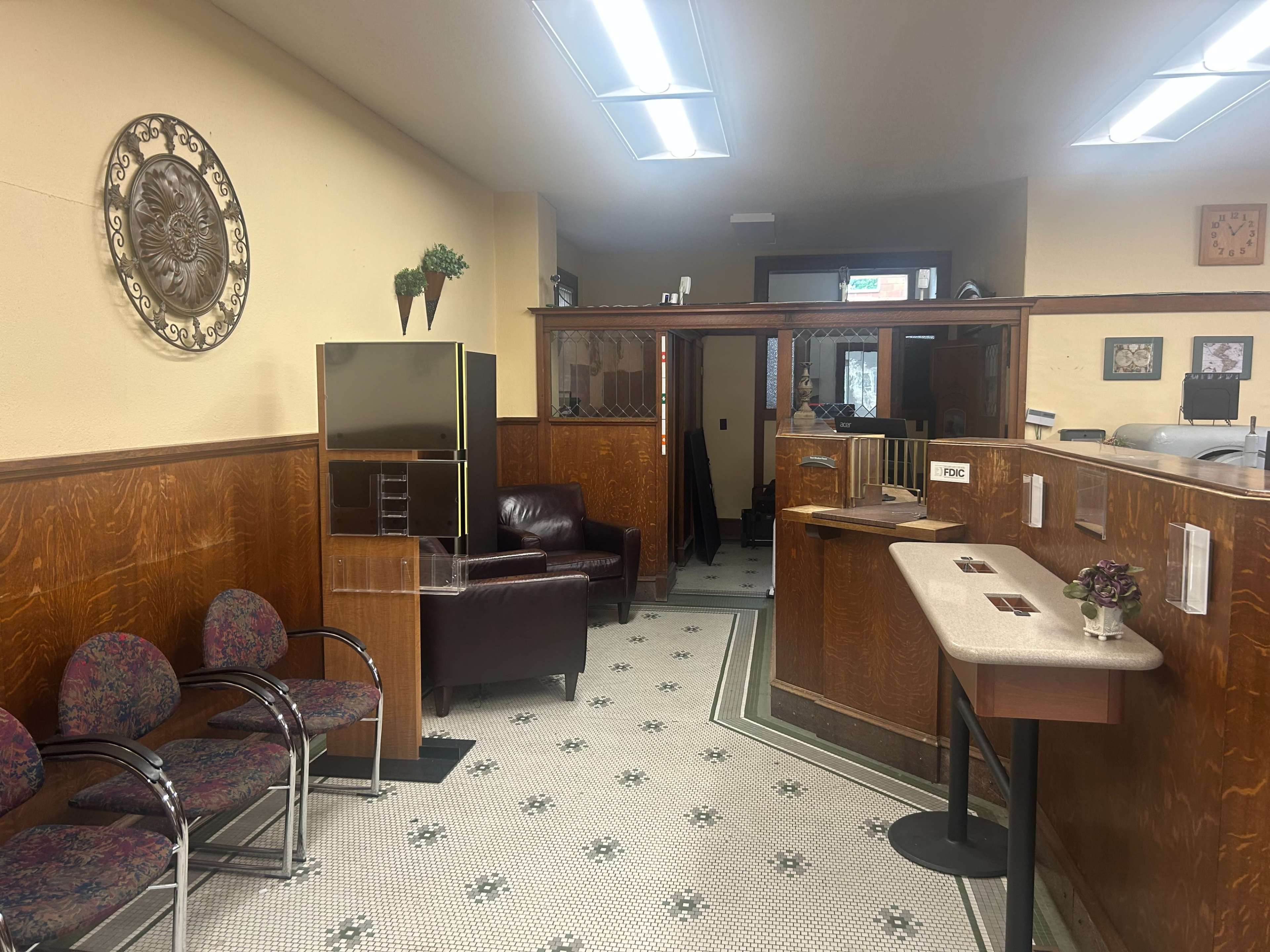 The image shows a waiting area with a brown leather chair, patterned seating, wood-paneled walls, and a tiled floor, featuring a reception desk and decorative wall art.